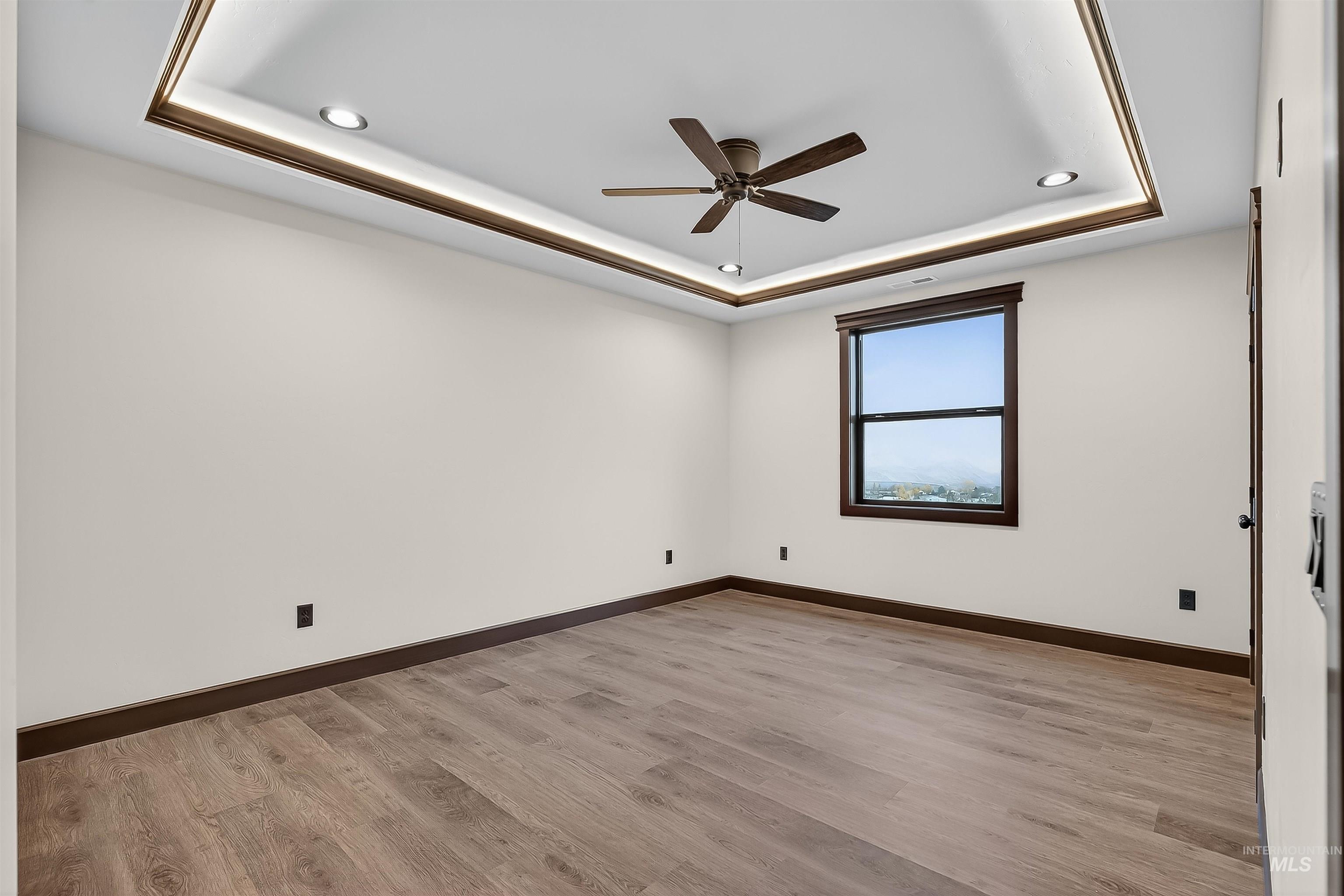 Empty room featuring a raised ceiling, light wood-style flooring, a ceiling fan, and recessed lighting