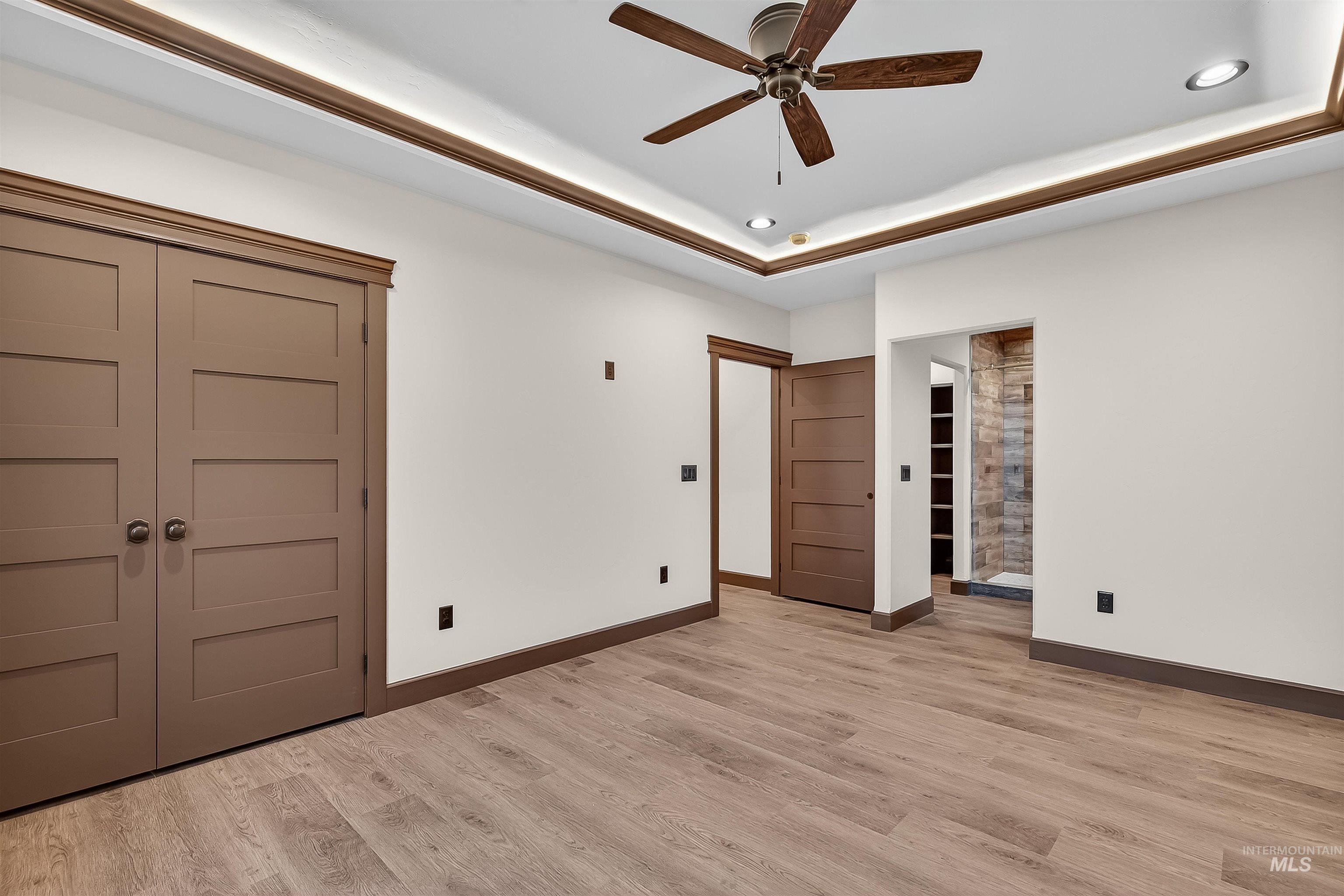 Unfurnished bedroom featuring ensuite bathroom, light wood-style floors, a ceiling fan, and a tray ceiling