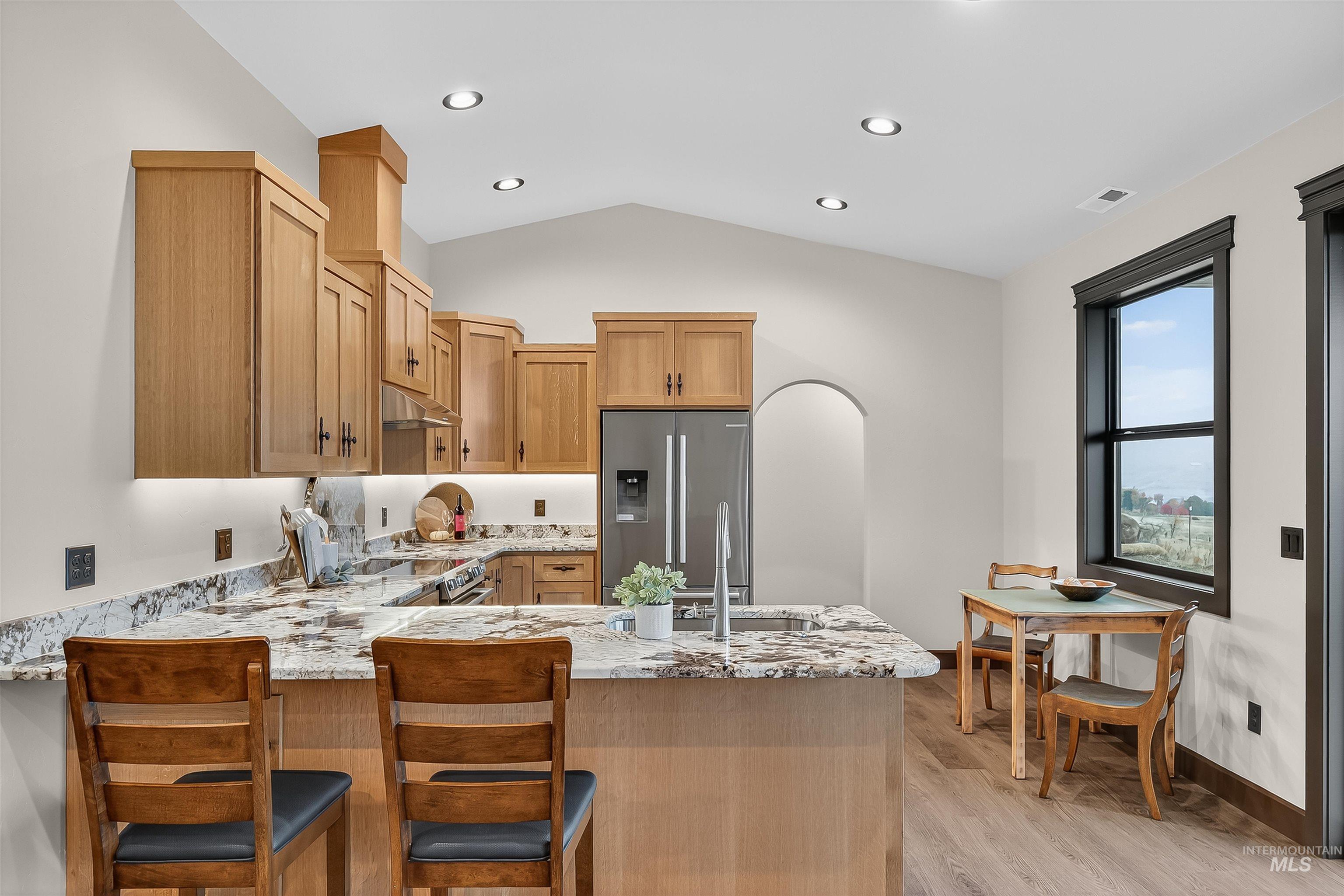 Kitchen featuring light stone counters, appliances with stainless steel finishes, a peninsula, light wood-style floors, and vaulted ceiling