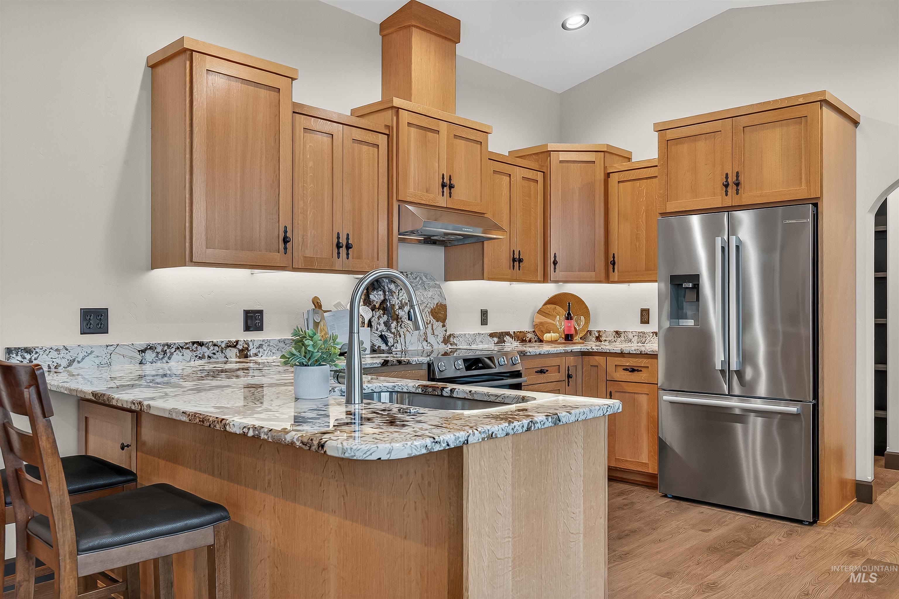 Kitchen featuring light stone countertops, stainless steel refrigerator with ice dispenser, a peninsula, a kitchen breakfast bar, and light wood-type flooring