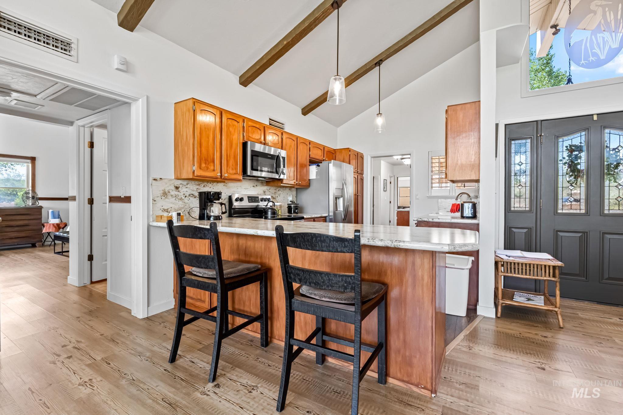 Kitchen featuring stainless steel appliances, a peninsula, beam ceiling, backsplash, and light wood-type flooring