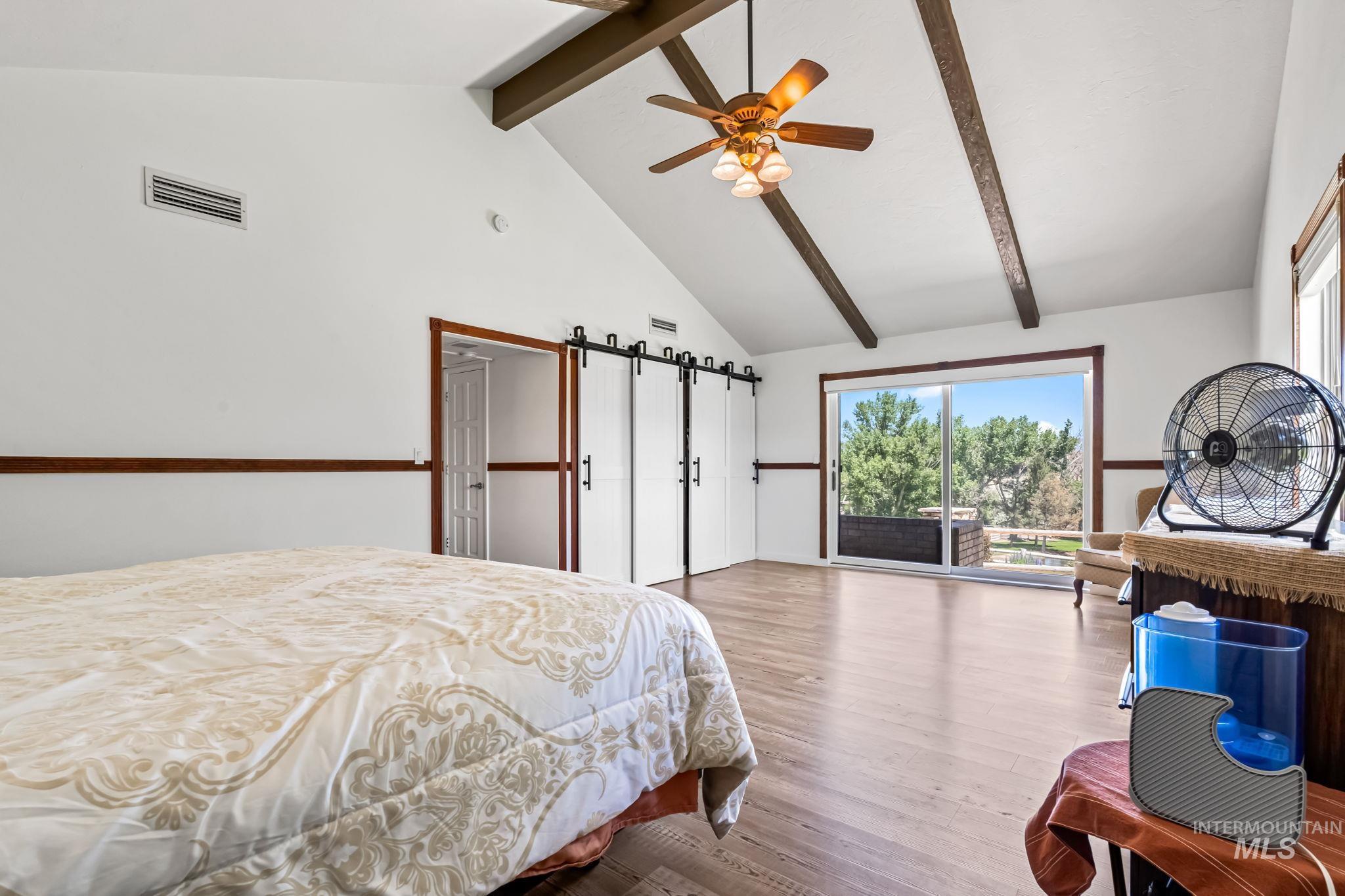 Bedroom featuring beamed ceiling, access to exterior, wood finished floors, multiple windows, and high vaulted ceiling