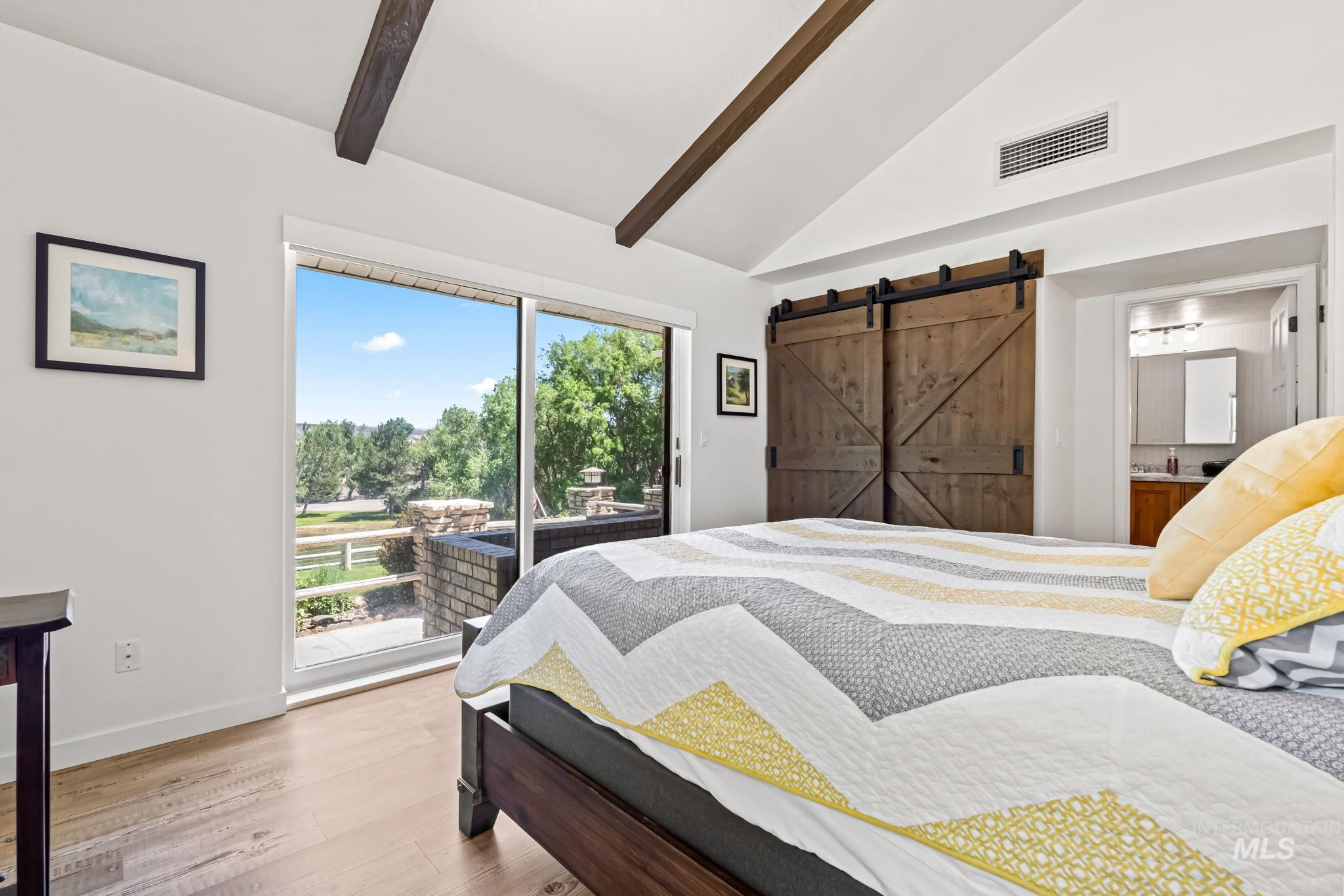 Bedroom featuring access to outside, a barn door, wood finished floors, beam ceiling, and ensuite bath