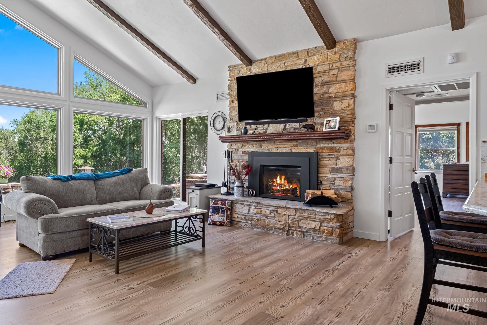 Living room with beamed ceiling, a stone fireplace, wood finished floors, and high vaulted ceiling