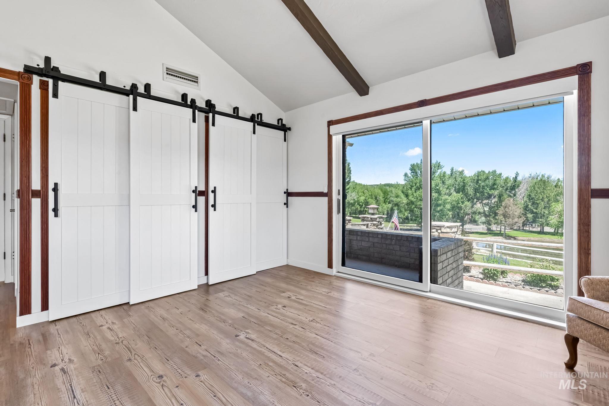Unfurnished bedroom with a barn door, wood finished floors, and access to outside