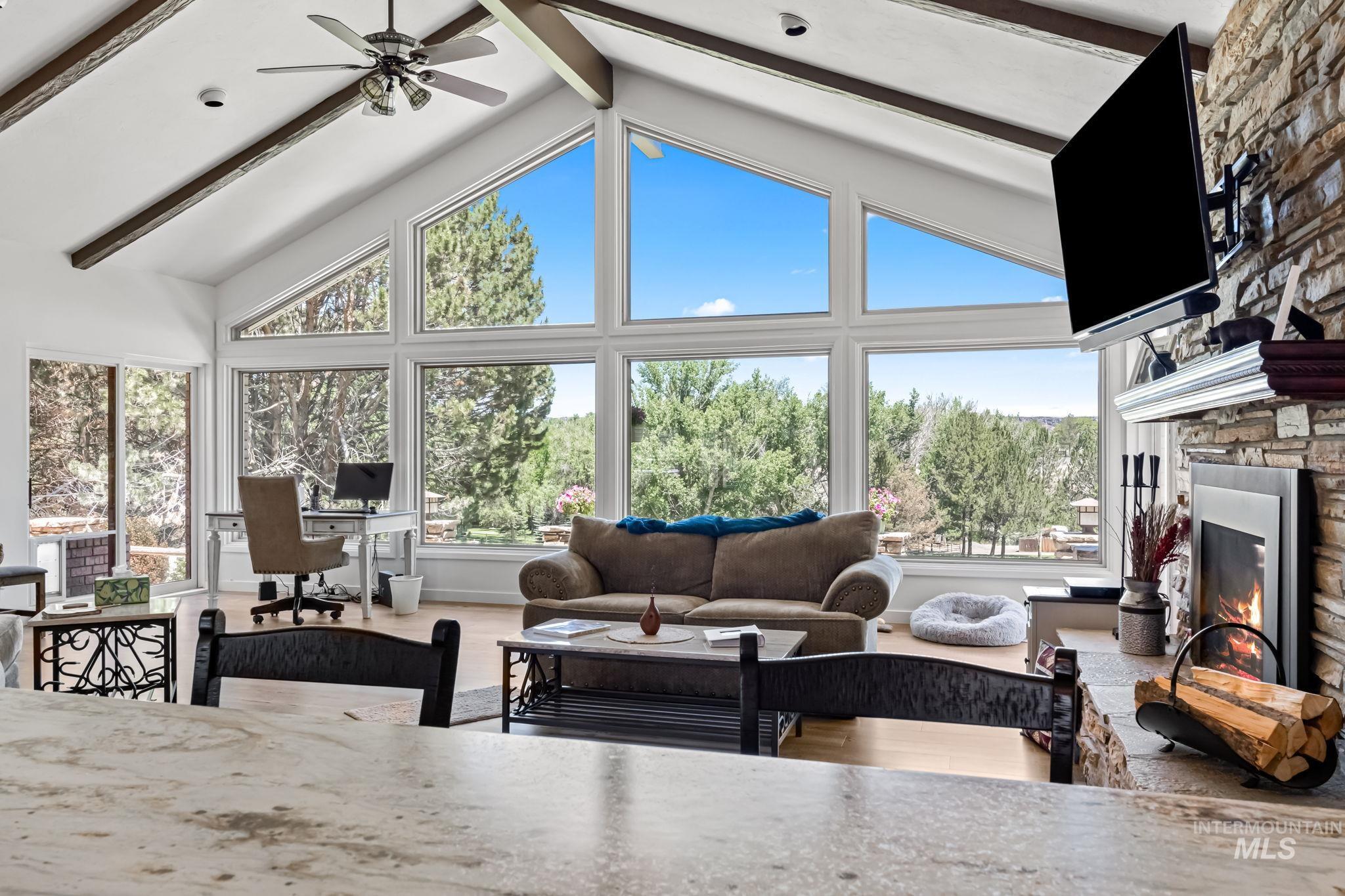 Living room featuring wood finished floors, a fireplace, a ceiling fan, a desk, and beamed ceiling