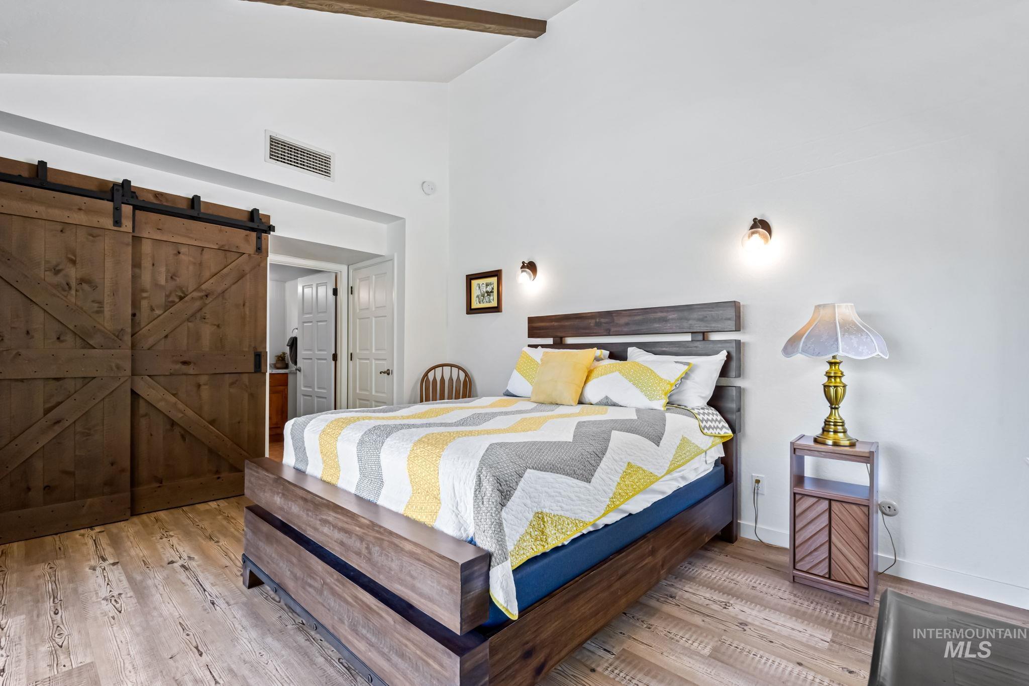Bedroom featuring wood finished floors, a barn door, beamed ceiling, and high vaulted ceiling