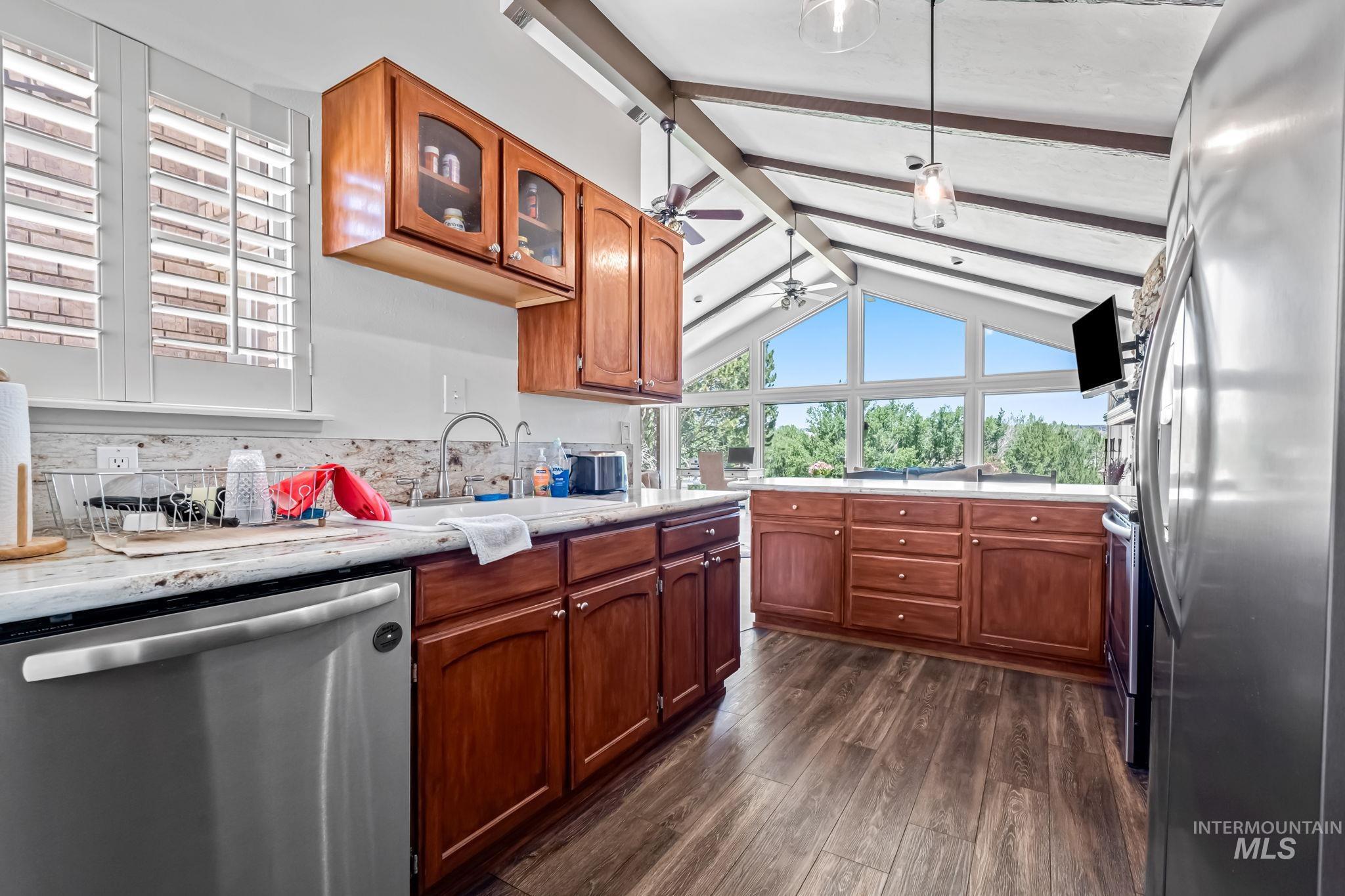 Kitchen featuring appliances with stainless steel finishes, a ceiling fan, dark wood-type flooring, glass insert cabinets, and brown cabinets