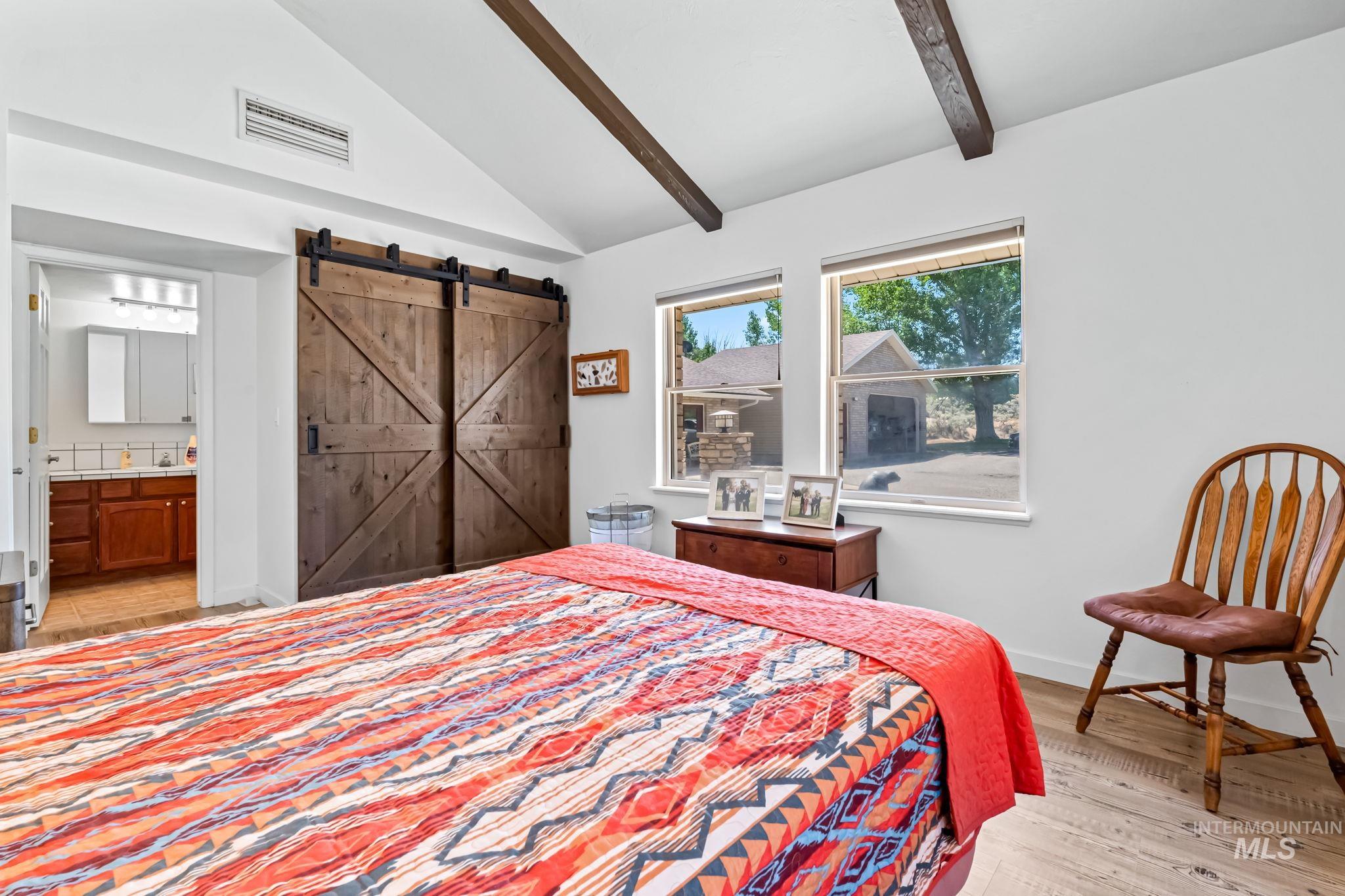 Bedroom featuring a barn door, light wood-style floors, and ensuite bathroom
