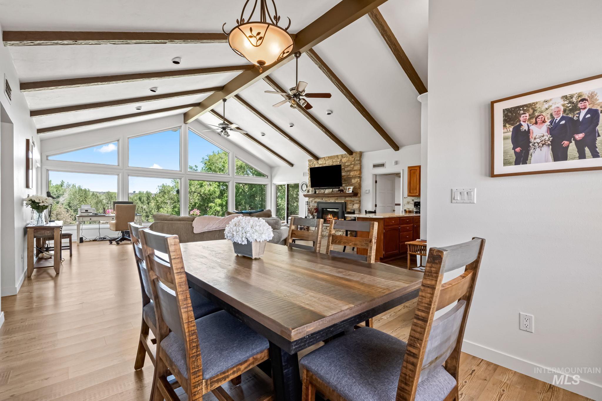 Dining area featuring a stone fireplace, a ceiling fan, beamed ceiling, light wood-type flooring, and high vaulted ceiling