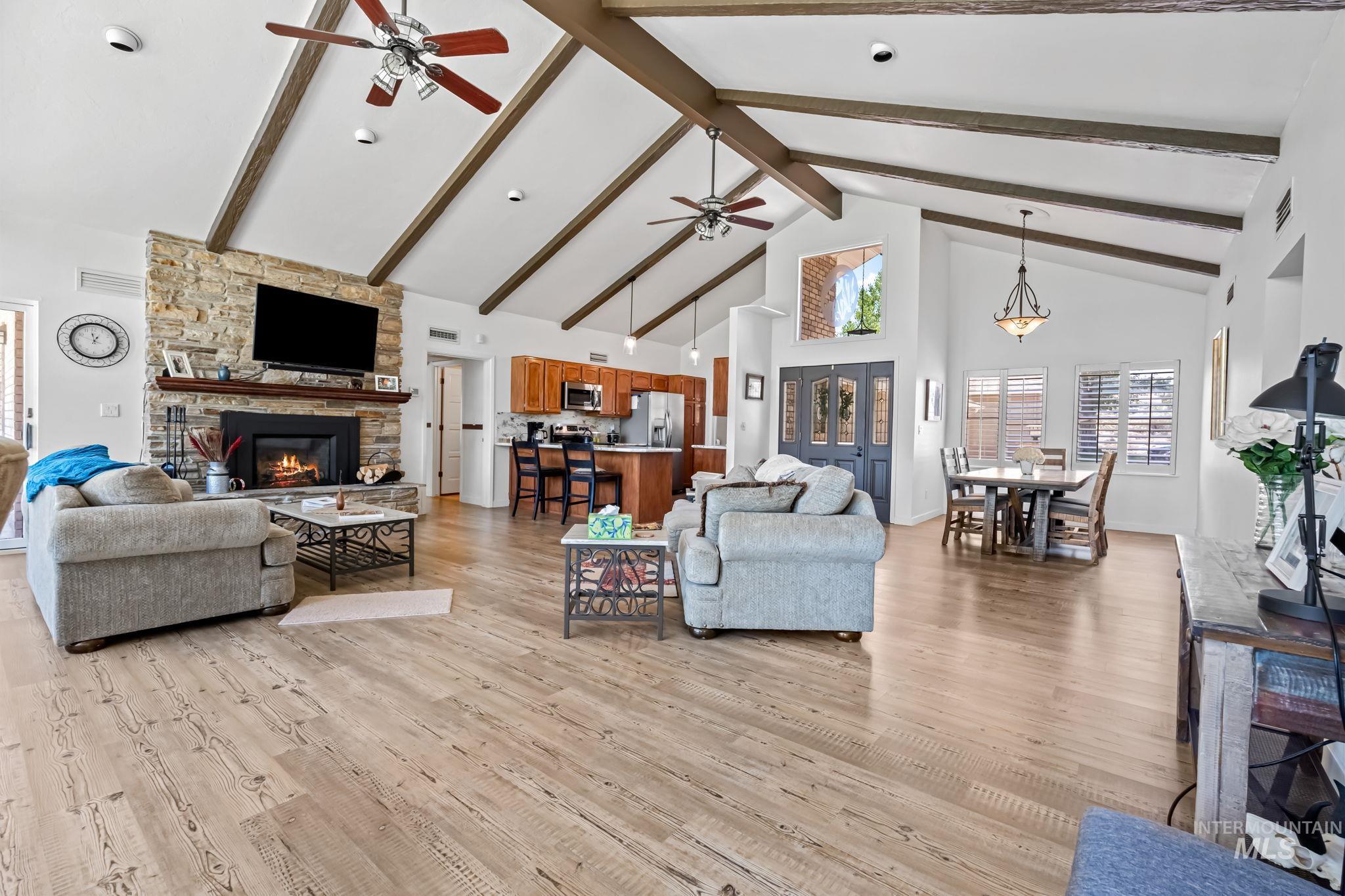Living room with a ceiling fan, high vaulted ceiling, a stone fireplace, light wood-style floors, and beam ceiling
