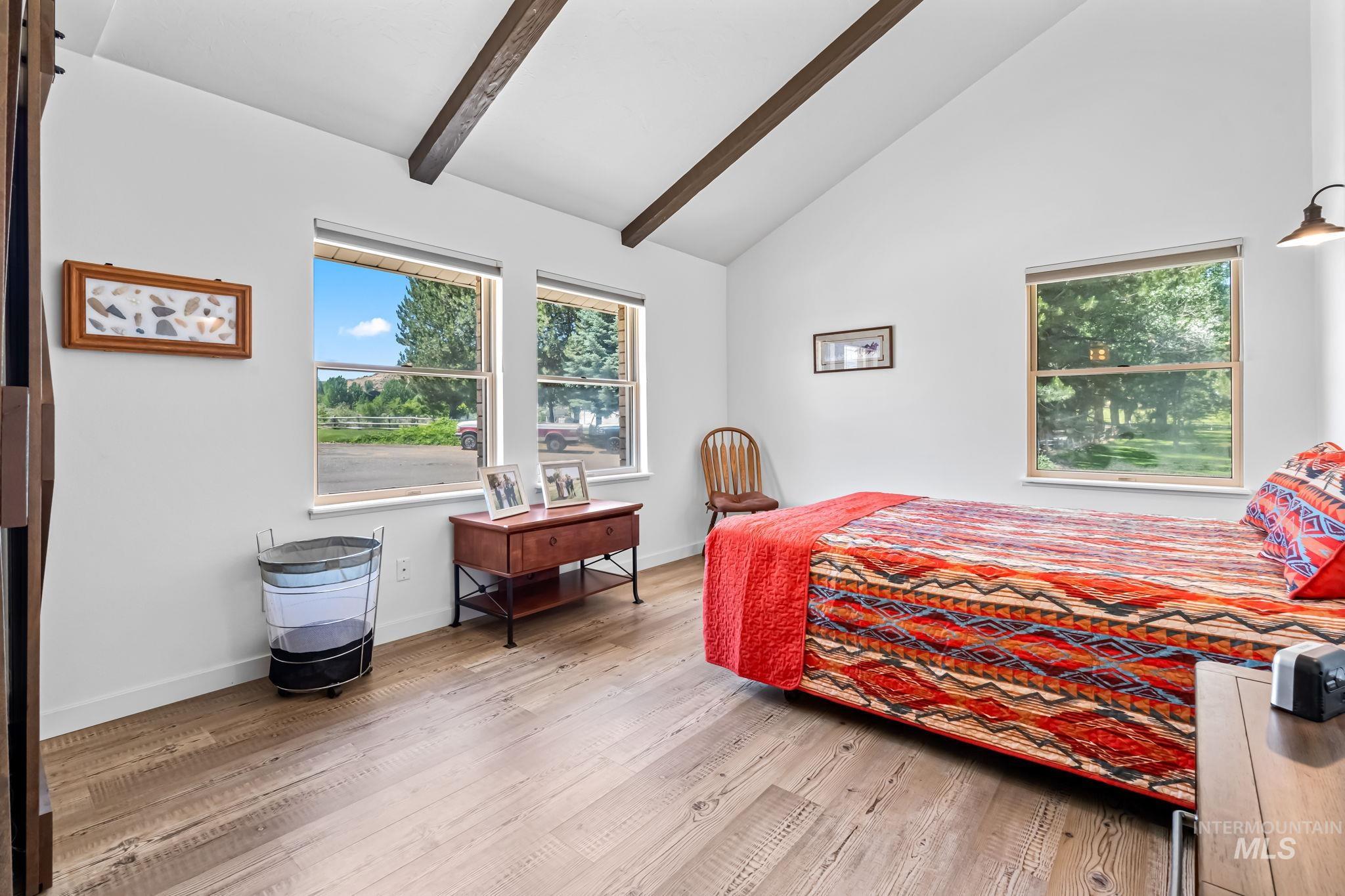 Bedroom with beam ceiling, multiple windows, wood finished floors, and high vaulted ceiling