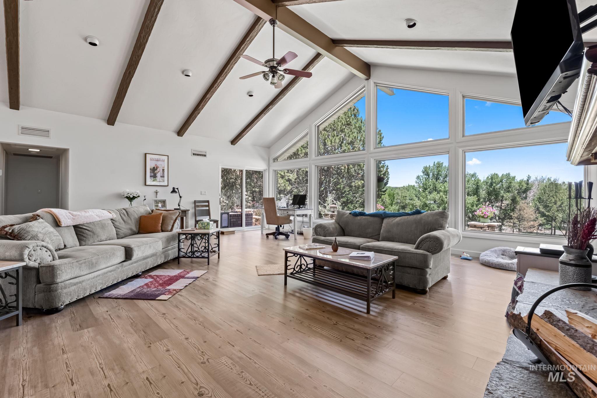 Living area with healthy amount of natural light, beam ceiling, light wood-type flooring, ceiling fan, and high vaulted ceiling