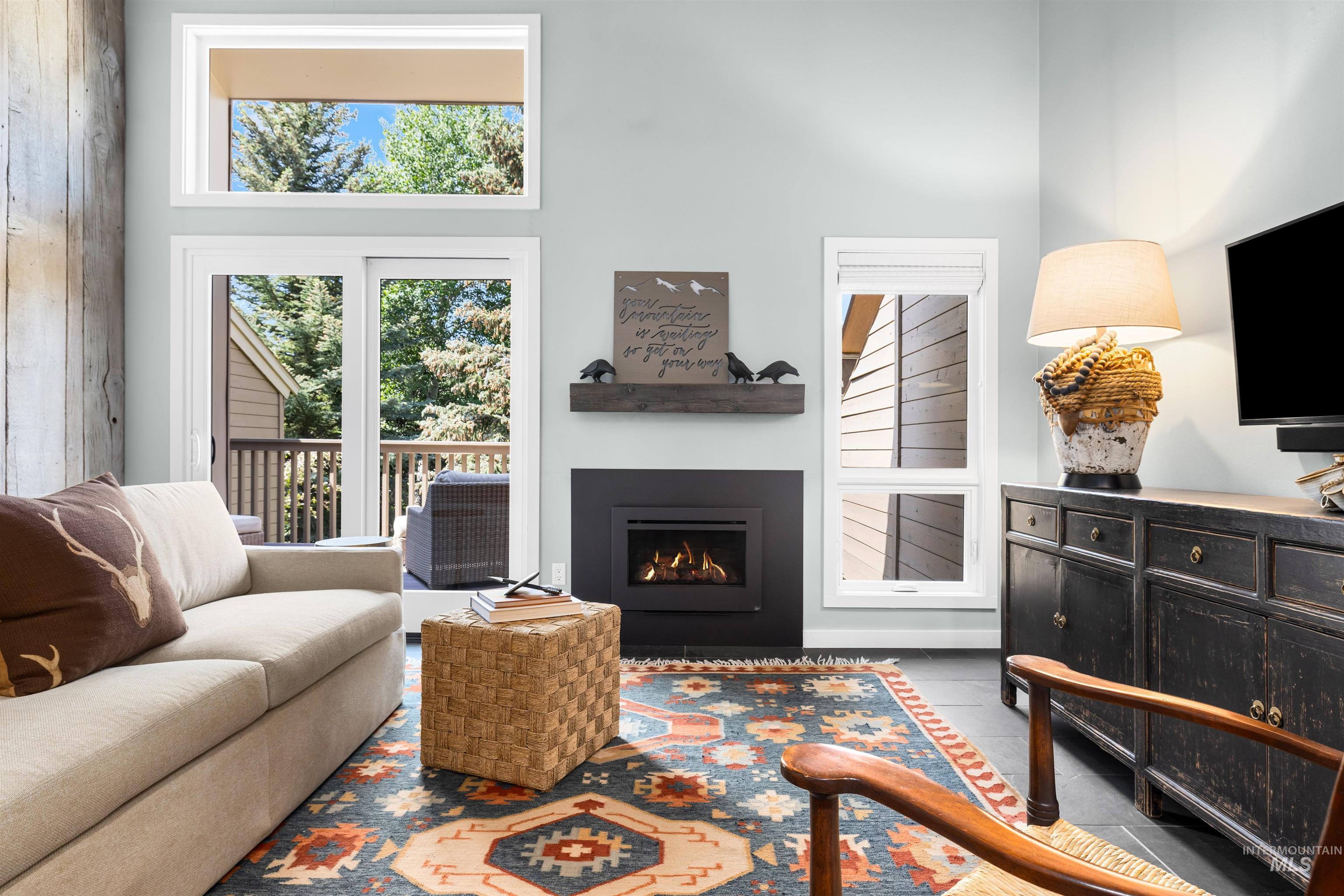 Tiled living area featuring a towering ceiling and a warm lit fireplace