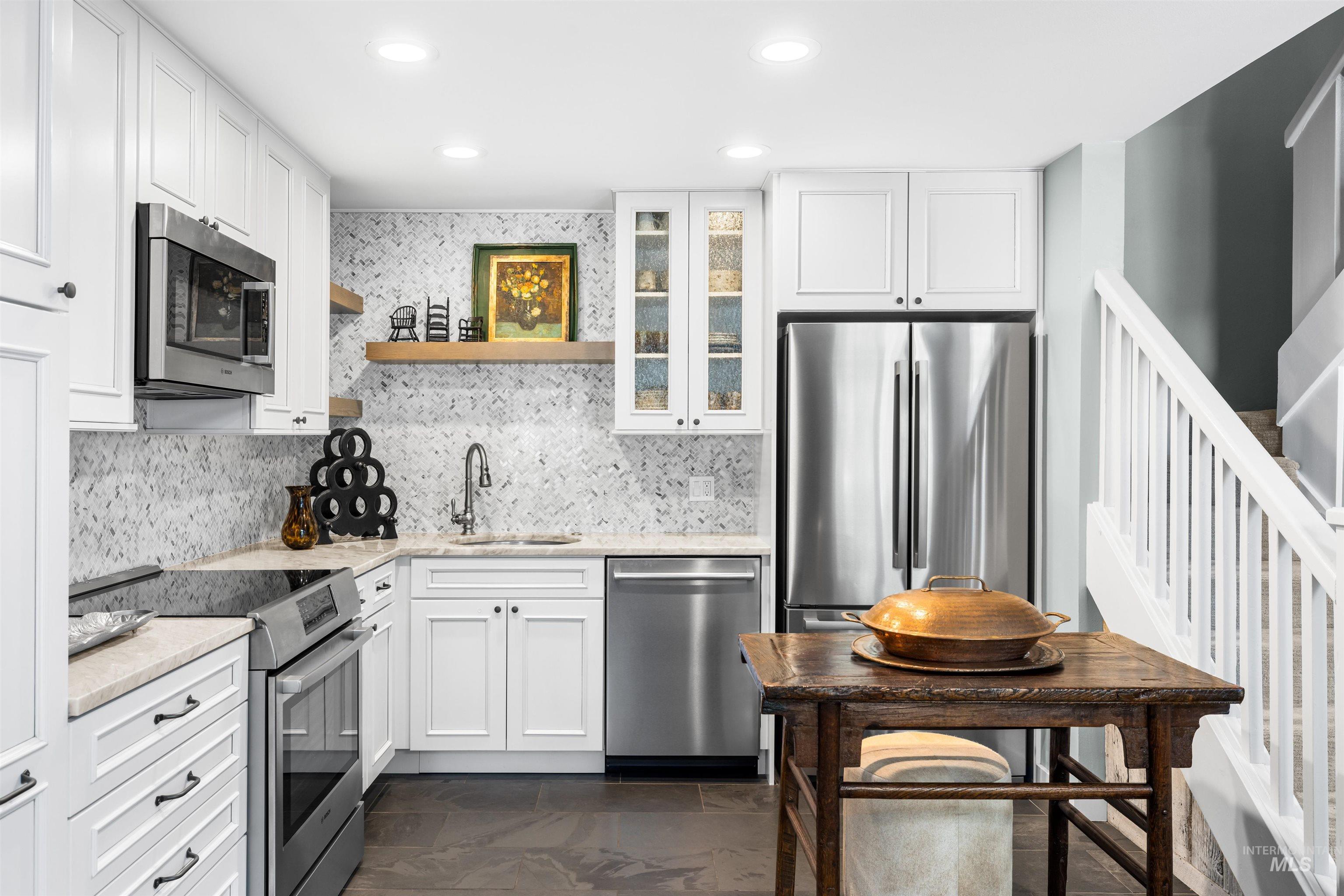 Kitchen with appliances with stainless steel finishes, tasteful backsplash, white cabinetry, light stone counters, and recessed lighting