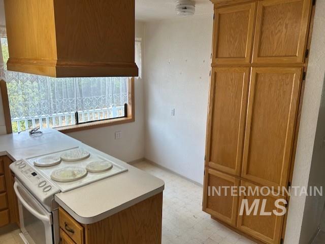 Kitchen featuring white range with electric stovetop, brown cabinetry, light flooring, light countertops, and a peninsula