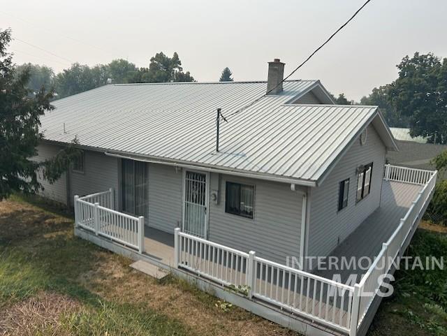 Rear view of house featuring a deck, a chimney, and a metal roof