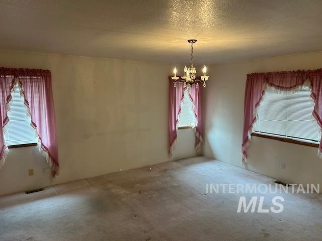 Unfurnished dining area featuring healthy amount of natural light, a textured ceiling, a chandelier, and carpet