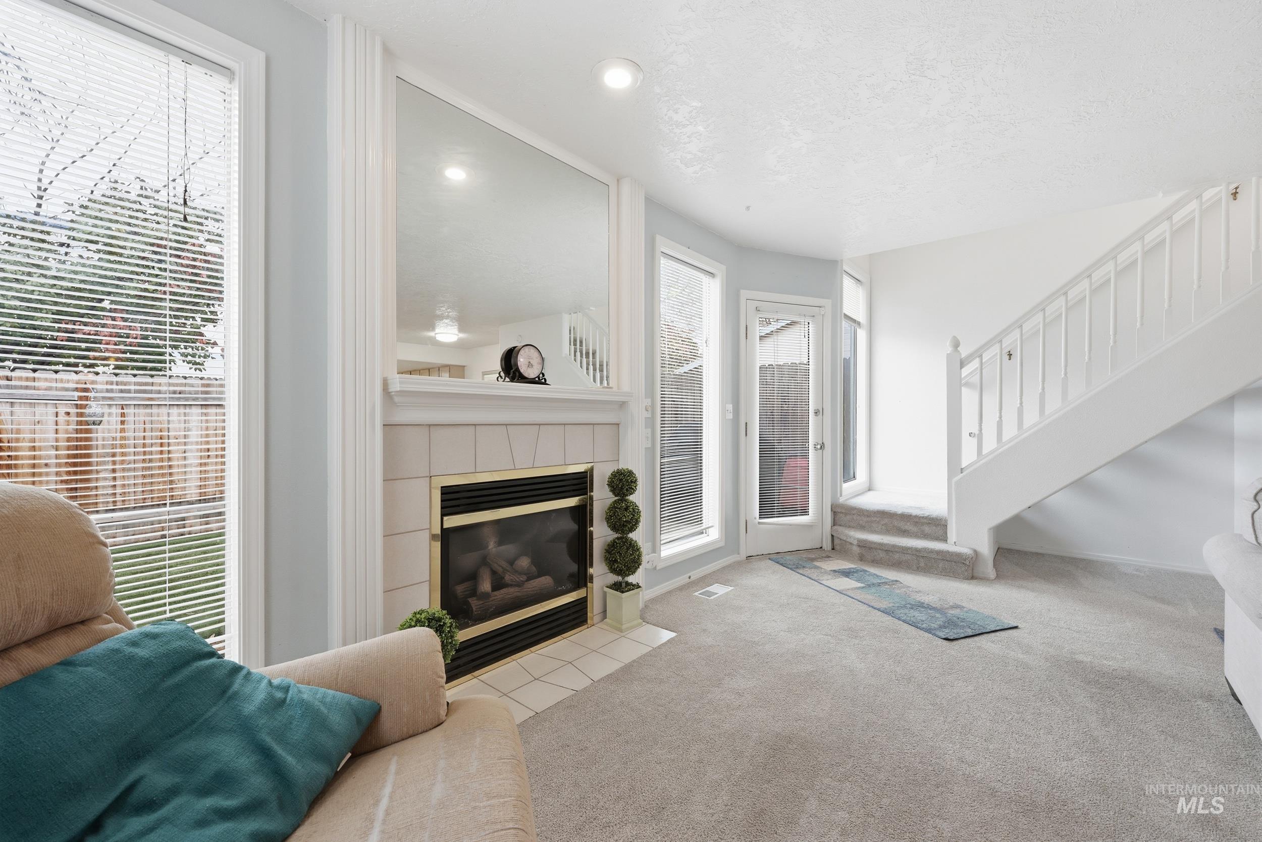 Carpeted living room featuring stairs, a tile fireplace, and recessed lighting