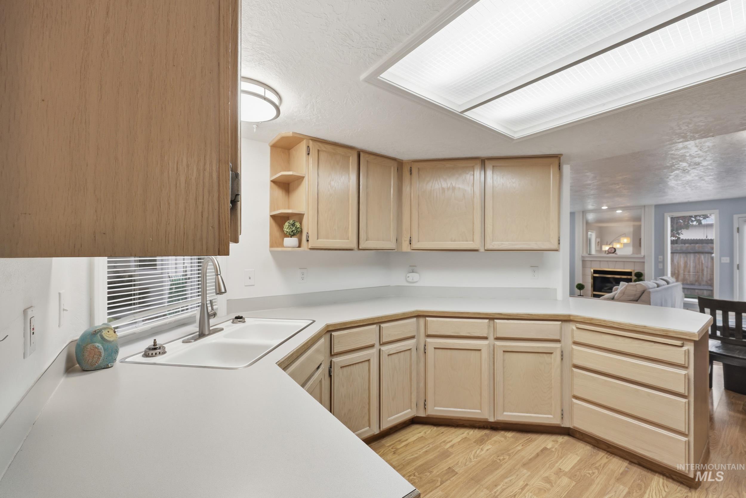Kitchen featuring light brown cabinets, open shelves, light countertops, a tile fireplace, and light wood-style floors