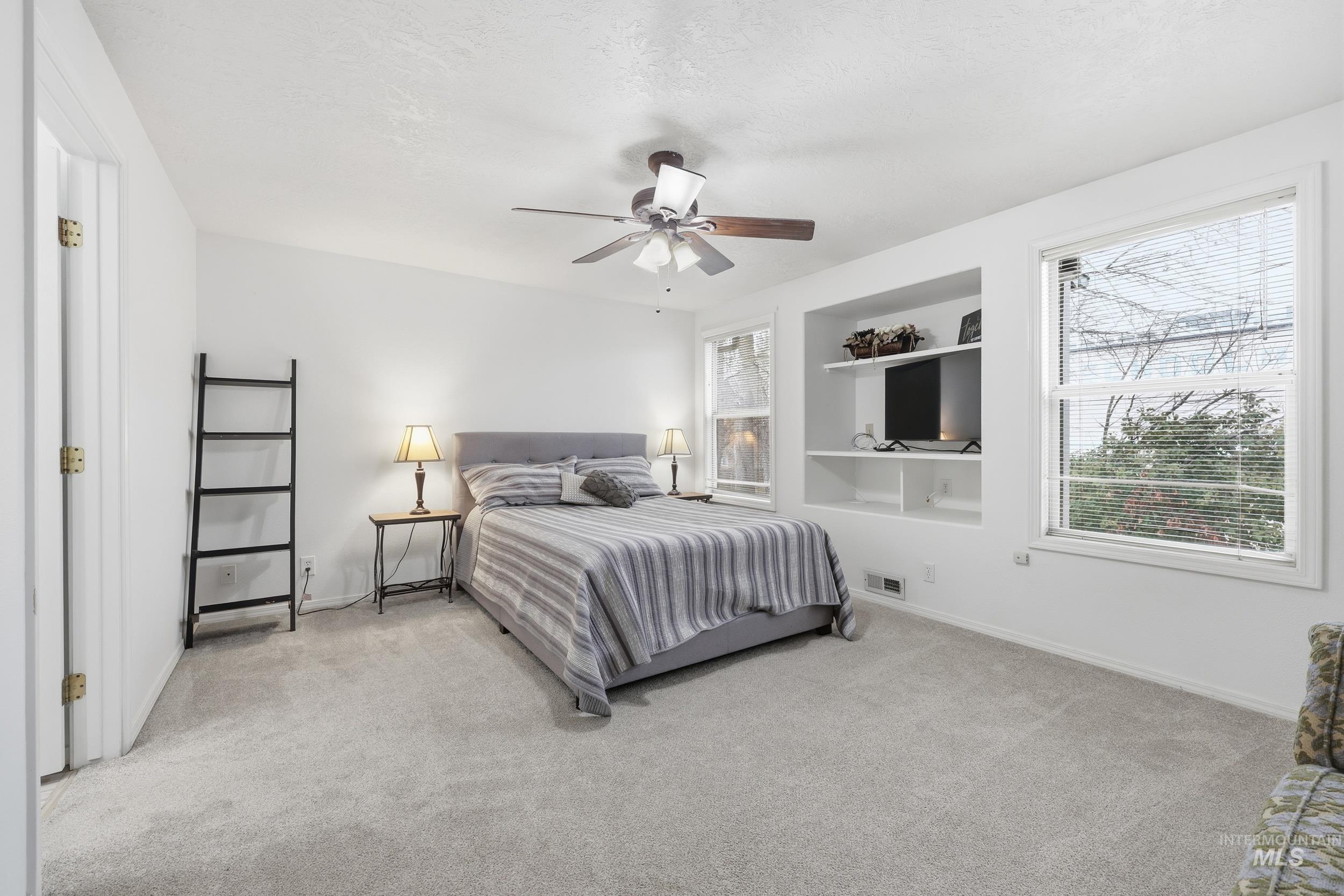 Carpeted bedroom with multiple windows, a ceiling fan, and a textured ceiling
