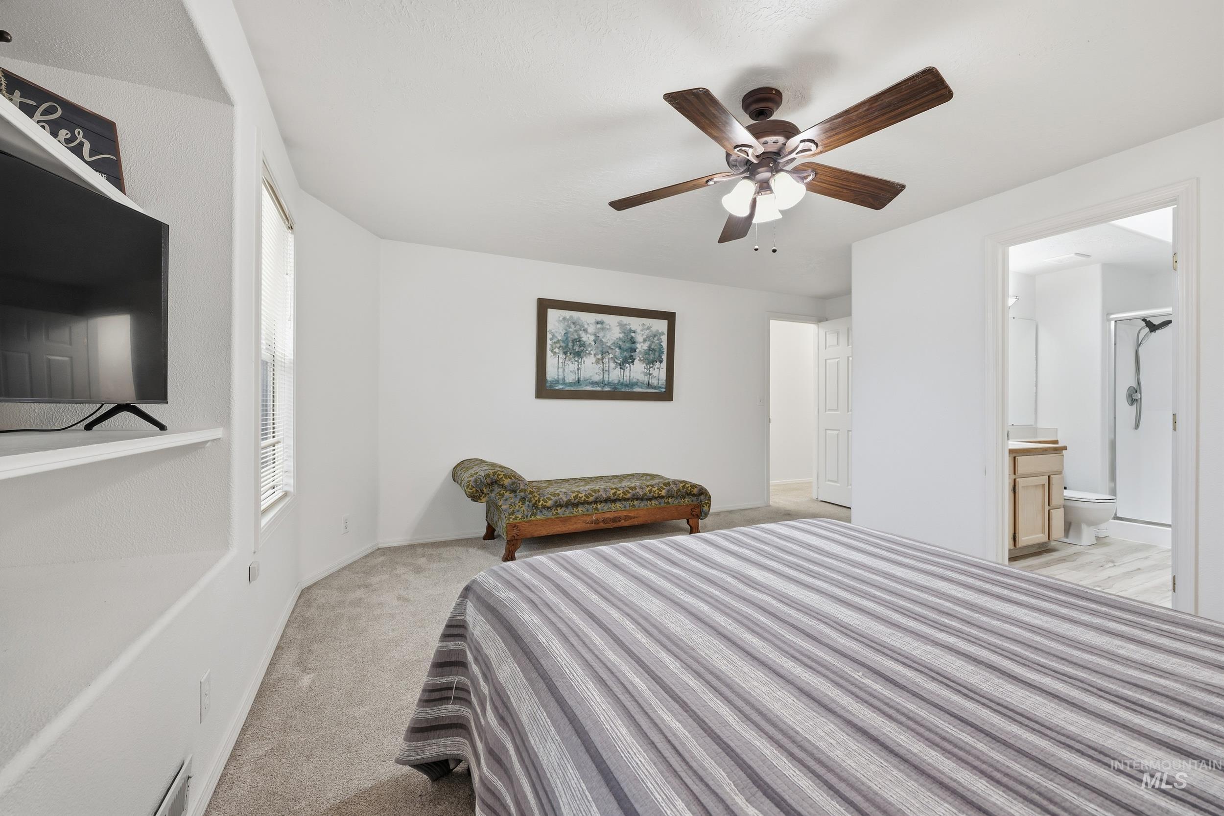 Bedroom with a ceiling fan, light colored carpet, and ensuite bathroom
