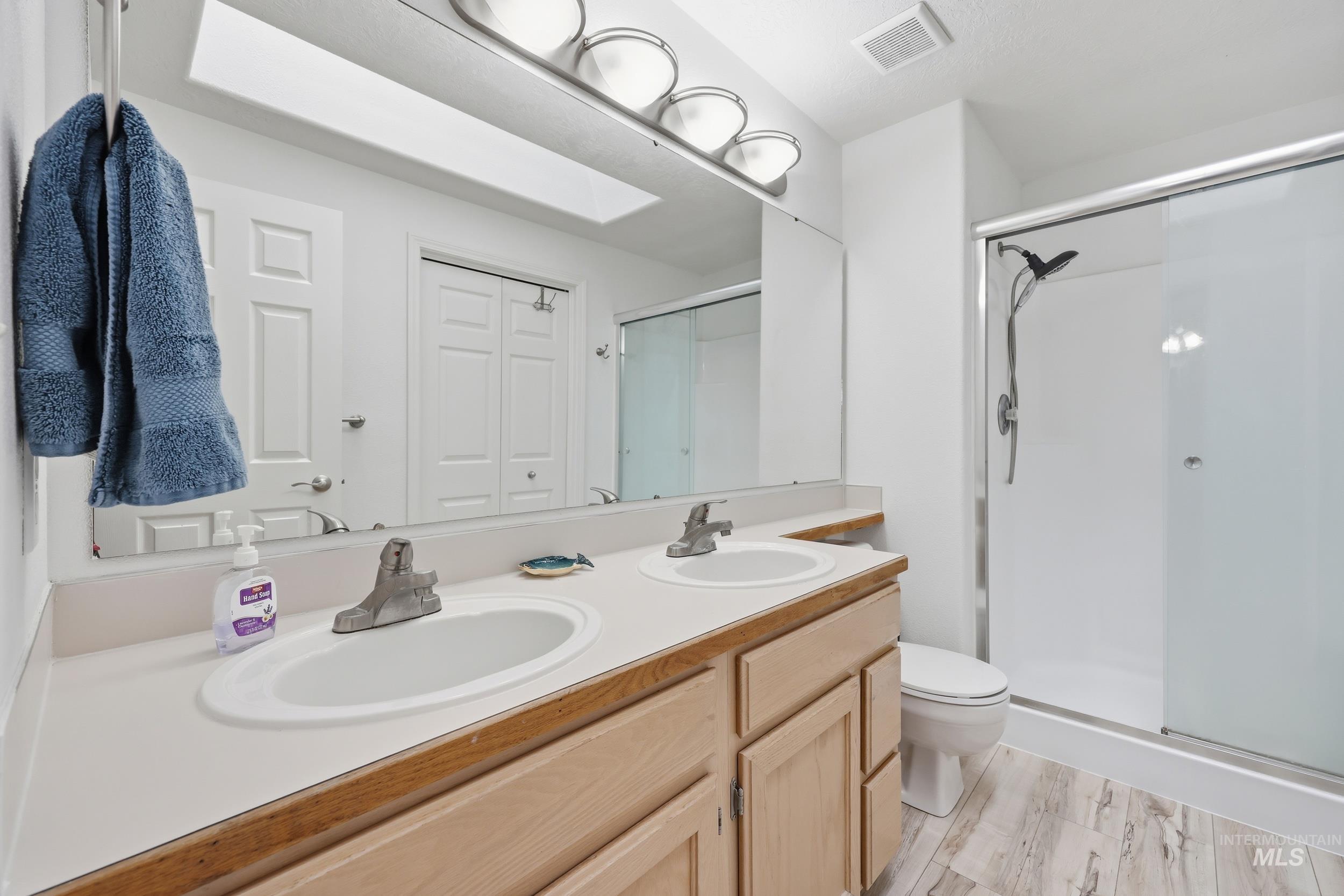 Bathroom with double vanity, a stall shower, and a closet