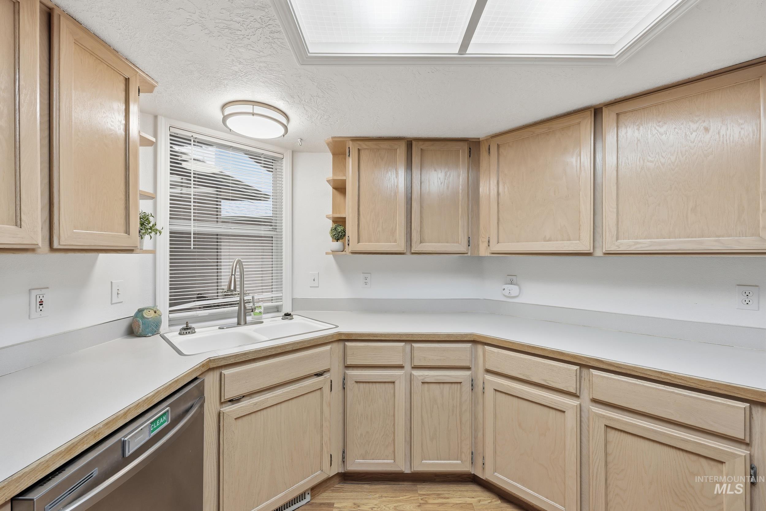 Kitchen featuring light brown cabinets, open shelves, light countertops, stainless steel dishwasher, and a textured ceiling
