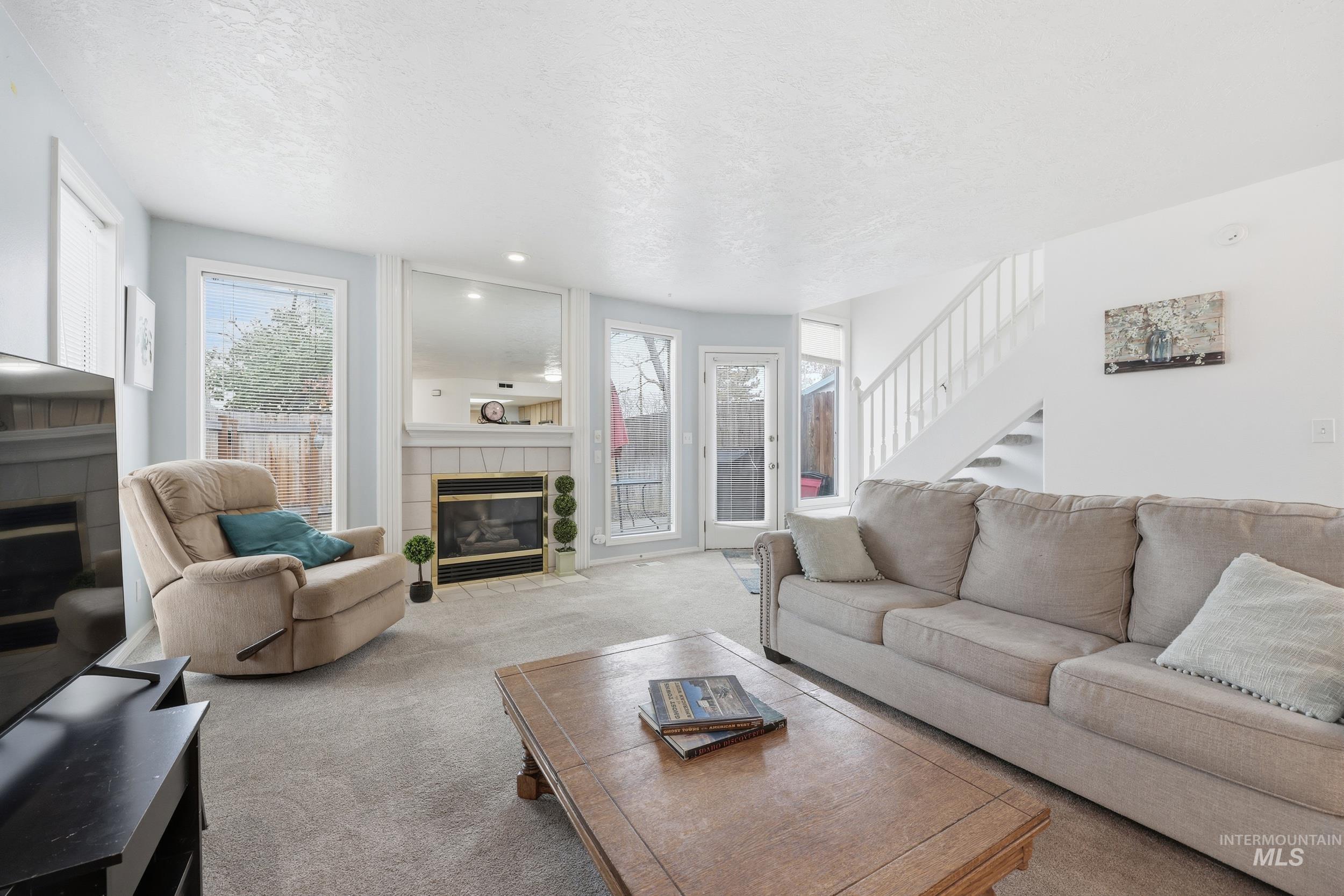 Carpeted living area featuring a tiled fireplace, stairway, and a textured ceiling