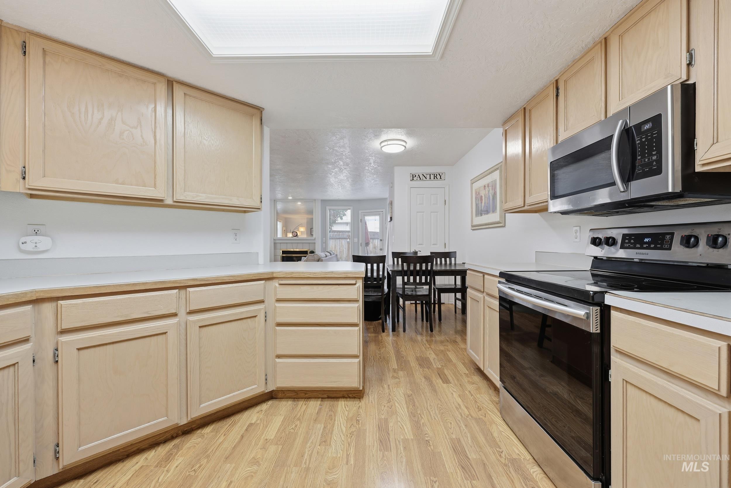Kitchen featuring light brown cabinetry, appliances with stainless steel finishes, light countertops, a peninsula, and light wood finished floors