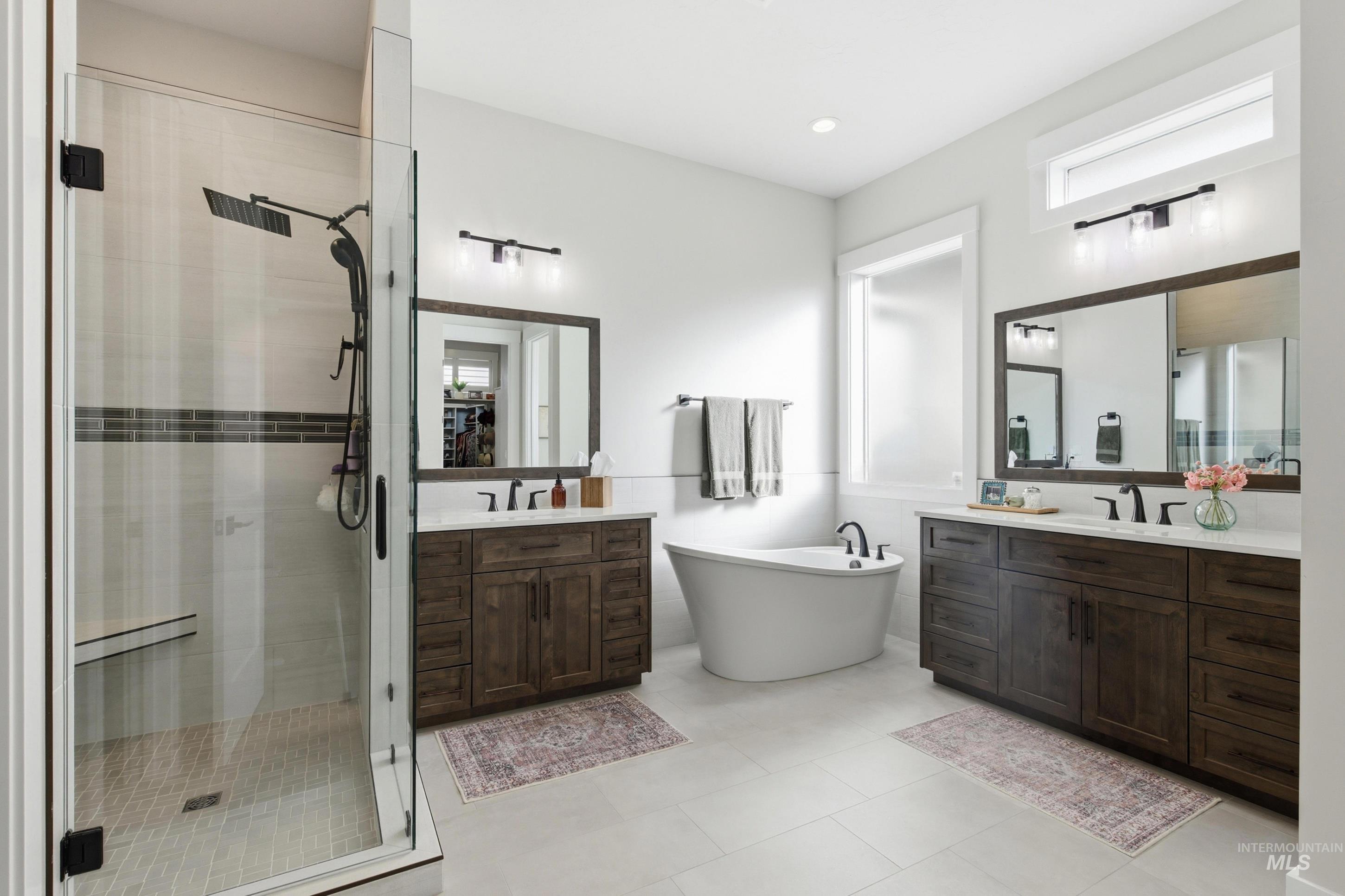 Bathroom featuring a shower stall, two vanities, a freestanding tub, and plenty of natural light