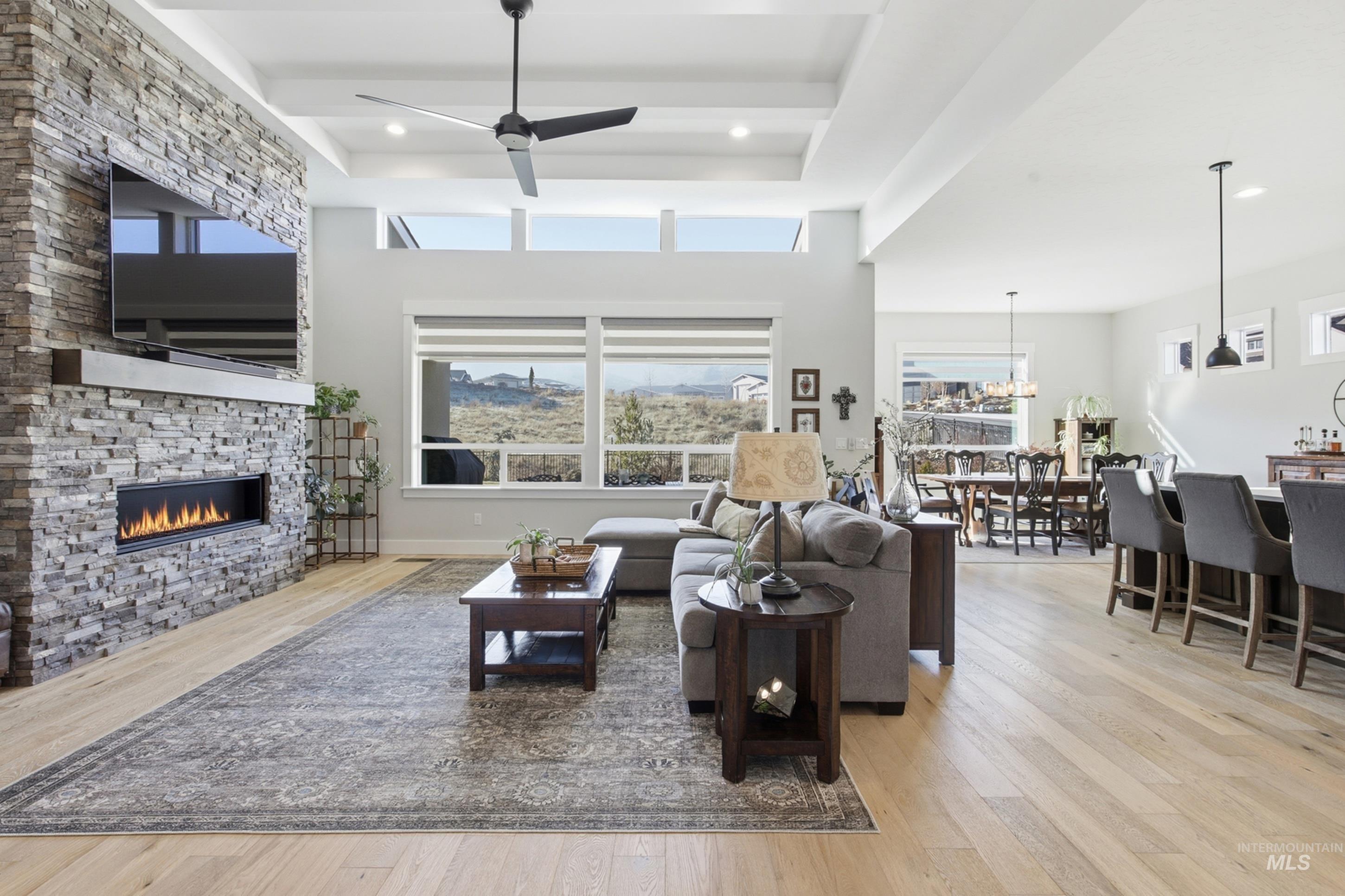 Living area featuring a stone fireplace, light wood finished floors, ceiling fan, a towering ceiling, and recessed lighting