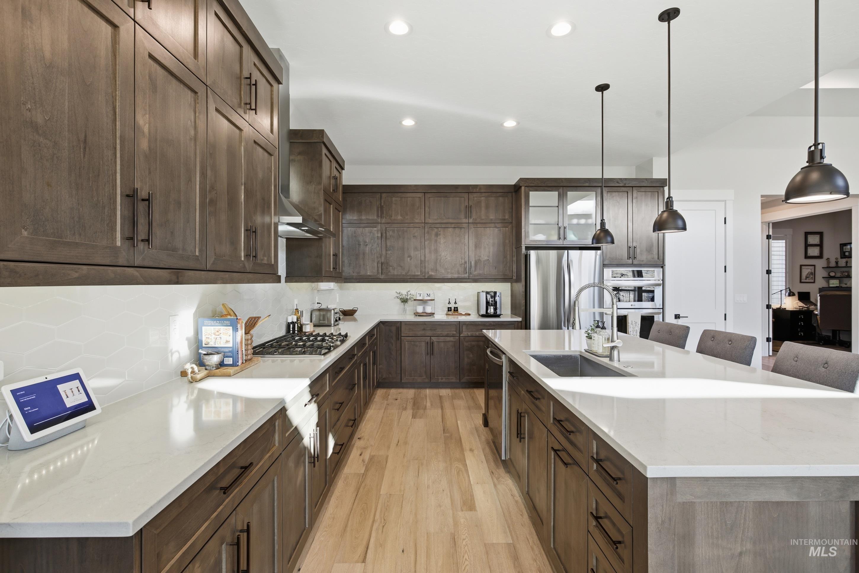 Kitchen featuring dark brown cabinetry, glass insert cabinets, light stone countertops, light wood-style flooring, and a breakfast bar