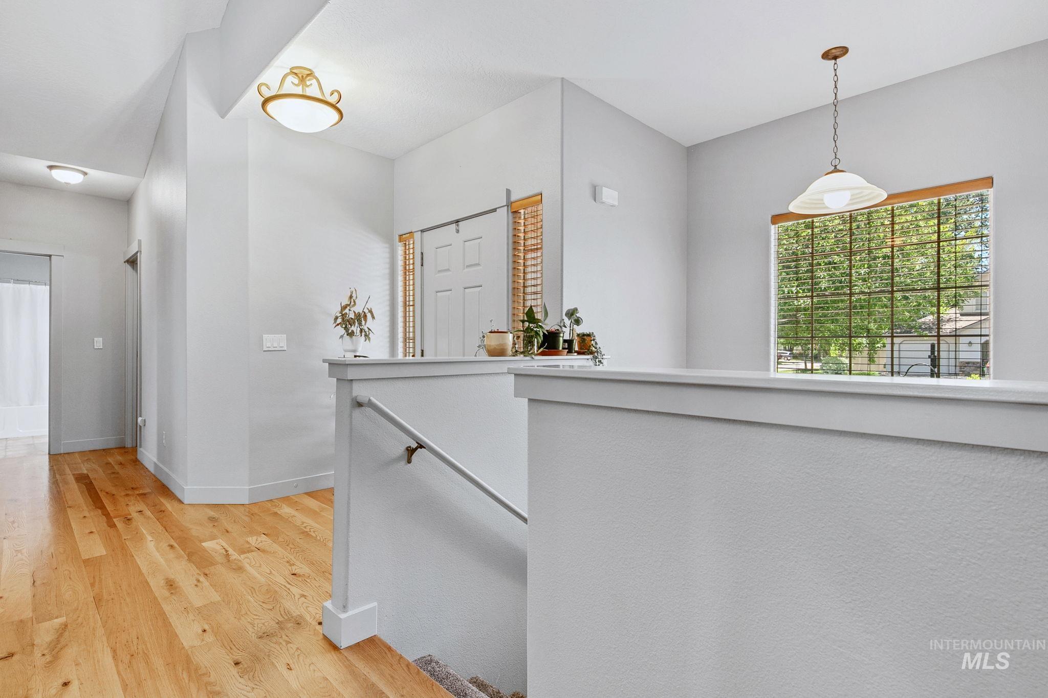 Upper-level landing featuring wood-finish flooring, light grey wall tones, a prominent window with wood-finish blinds, and a classic pendant light fixture
