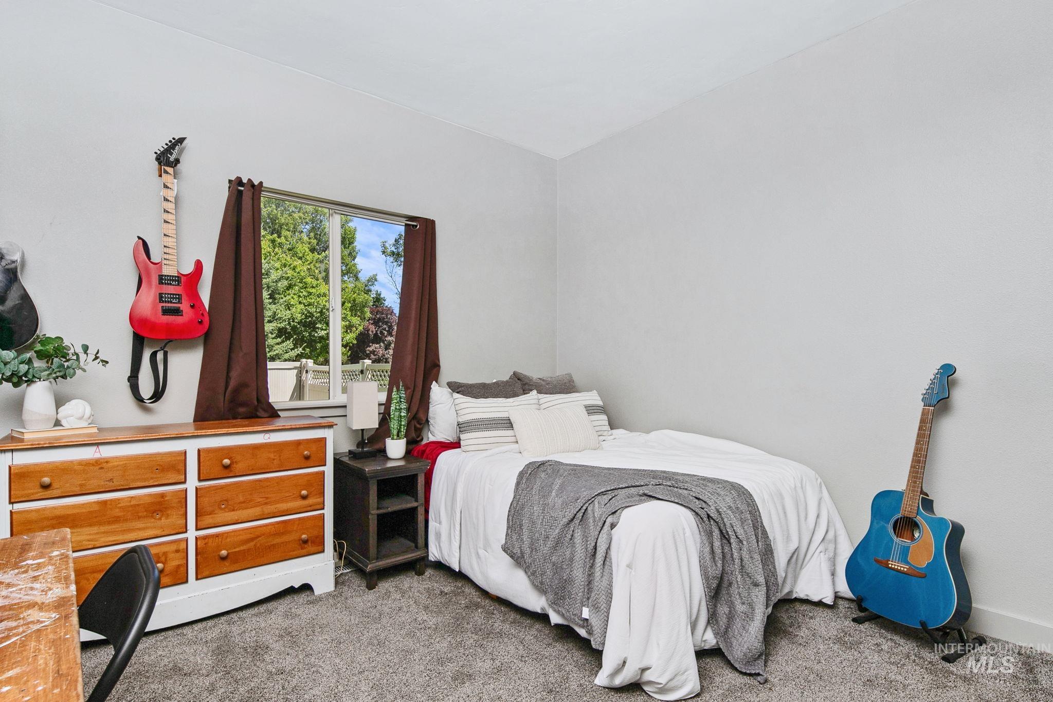 Bright interior room featuring a window with exterior green foliage, light-colored walls, and gray carpet flooring