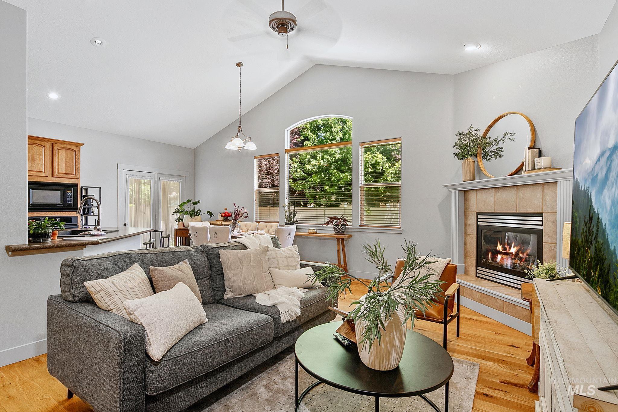 Living area featuring vaulted ceilings, wood-finish flooring, a tile-surround fireplace, large windows, and an open concept layout
