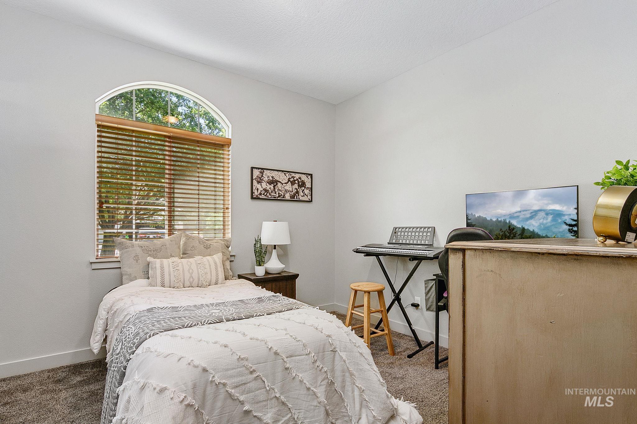 Room featuring a large arched window with horizontal blinds, neutral wall paint, and gray carpet flooring