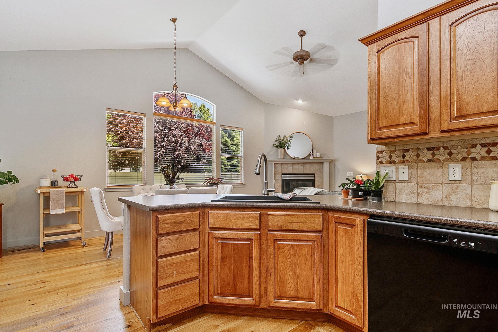 Kitchen island featuring wood-finish cabinetry, a black sink, and dark countertops, overlooking a dining area with wood-finish flooring