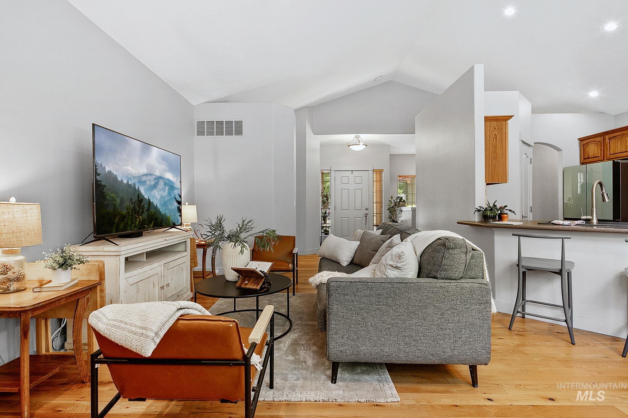 Open-concept living space featuring vaulted ceilings, wood-finish flooring, and a kitchen pass-through with a breakfast bar