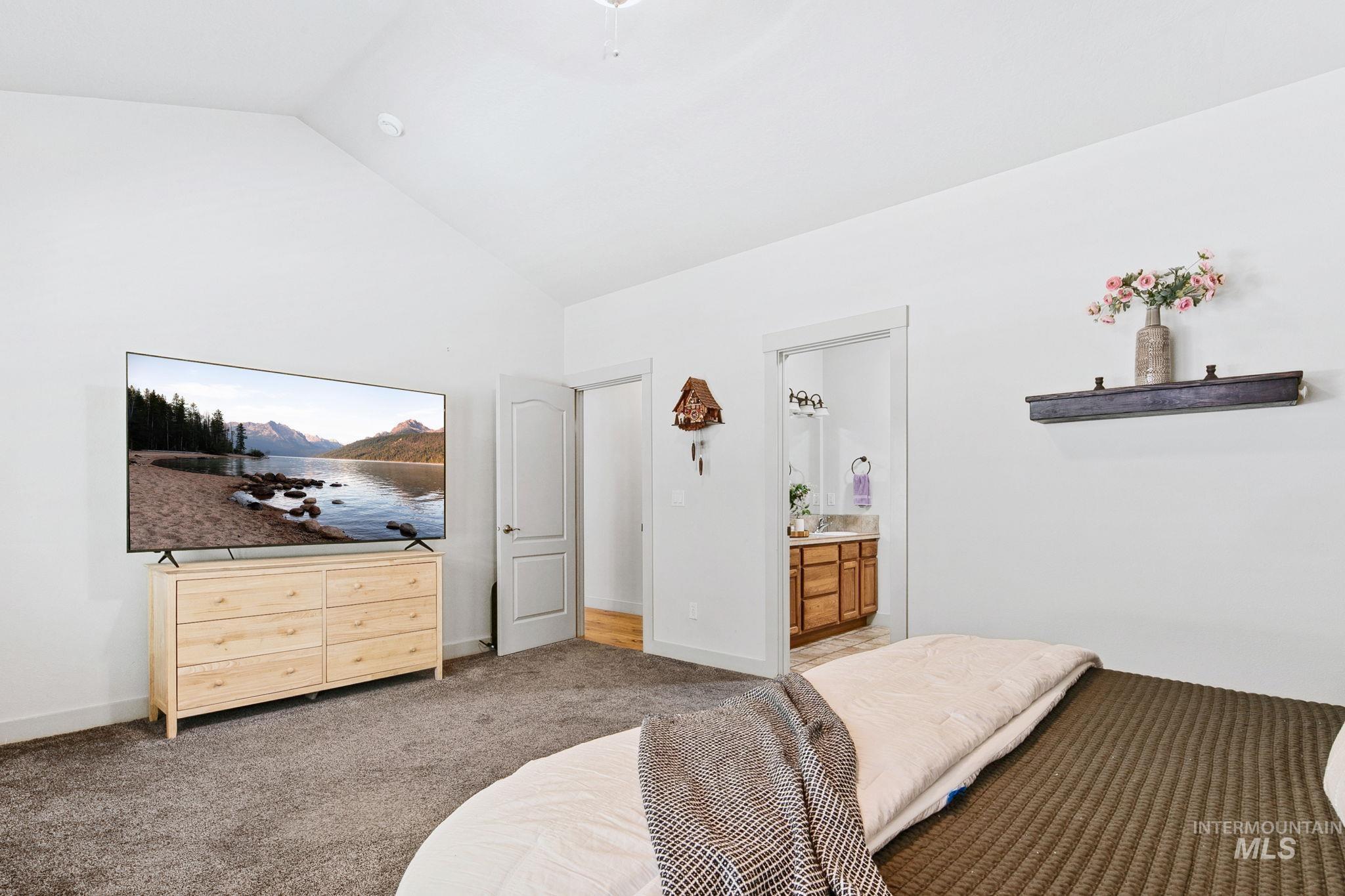 Carpeted room with a vaulted white ceiling, a white paneled door, and a wall-mounted wooden shelf