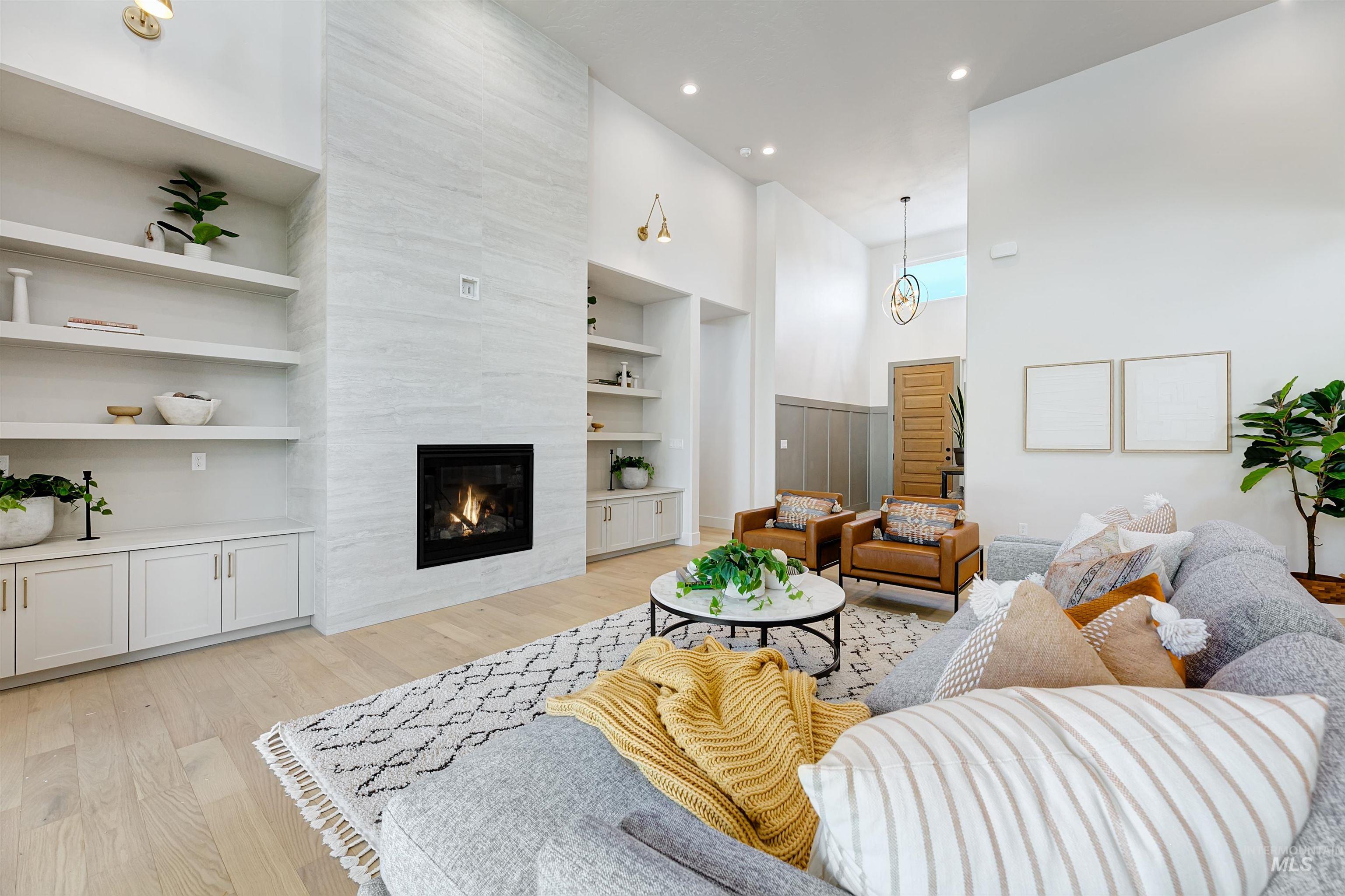 Living room featuring a towering ceiling, light wood finished floors, a fireplace, built in features, and recessed lighting
