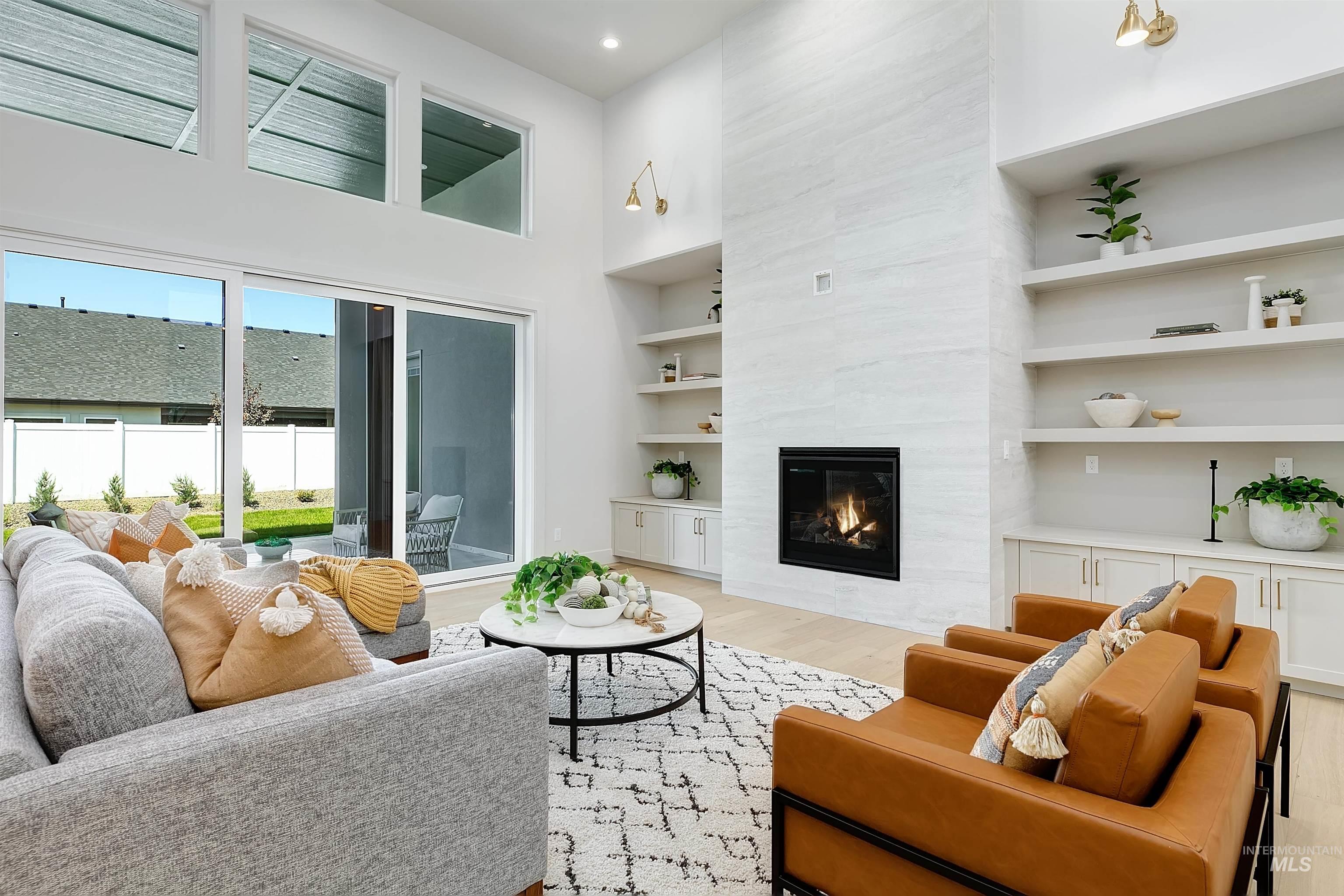 Living room with a towering ceiling, a tile fireplace, light wood-style flooring, built in shelves, and recessed lighting