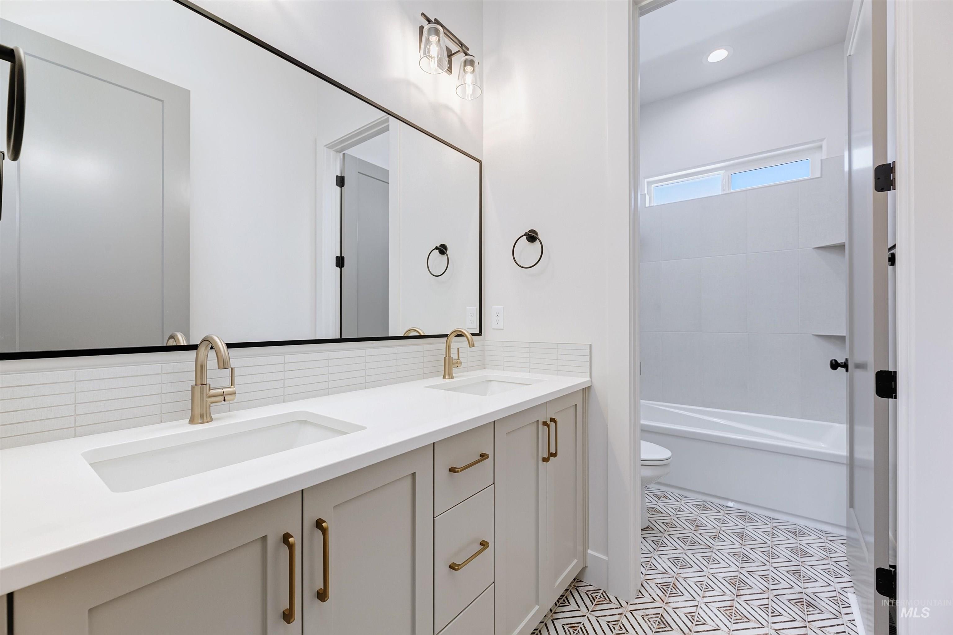 Bathroom with double vanity, backsplash, shower / bath combination, and recessed lighting