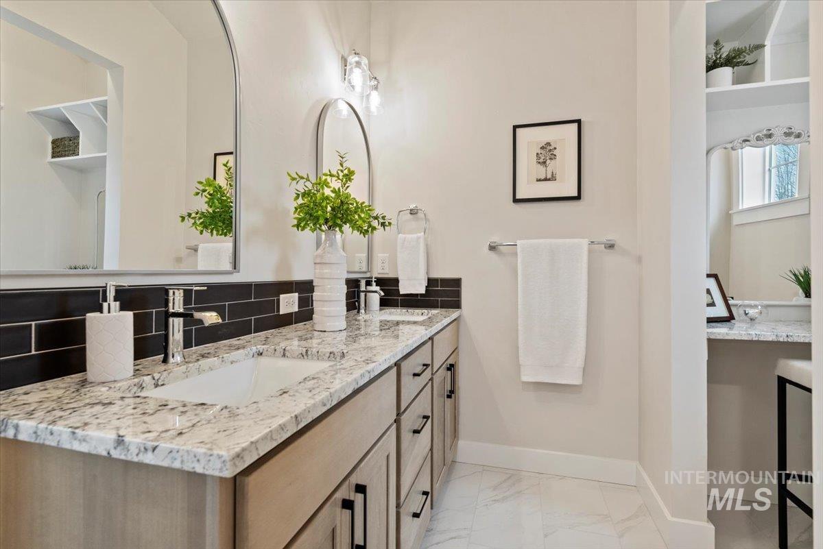 Full bathroom with double vanity, tasteful backsplash, and light marble finish floors