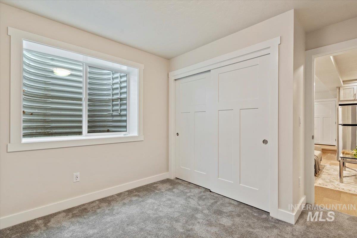 Unfurnished bedroom with freestanding refrigerator, a closet, and light carpet