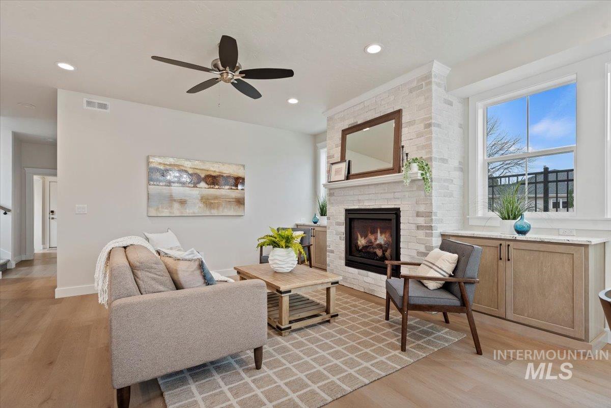 Living room featuring light wood-type flooring, a brick fireplace, a ceiling fan, and recessed lighting