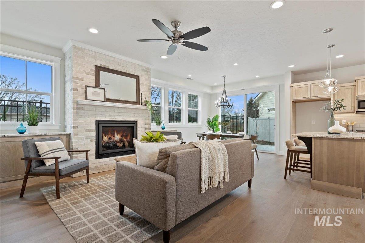 Living room with light wood-style floors, a fireplace, a chandelier, a ceiling fan, and recessed lighting
