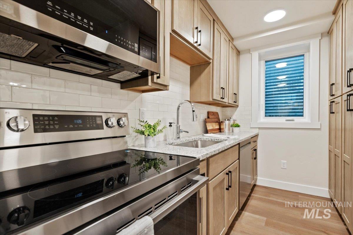 Kitchen featuring stainless steel appliances, light stone countertops, tasteful backsplash, light wood finished floors, and light brown cabinetry