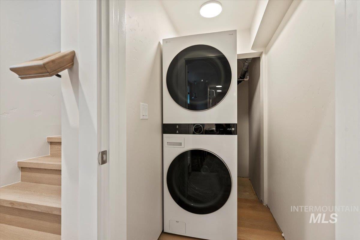 Laundry room with stacked washer / drying machine and light wood-style flooring