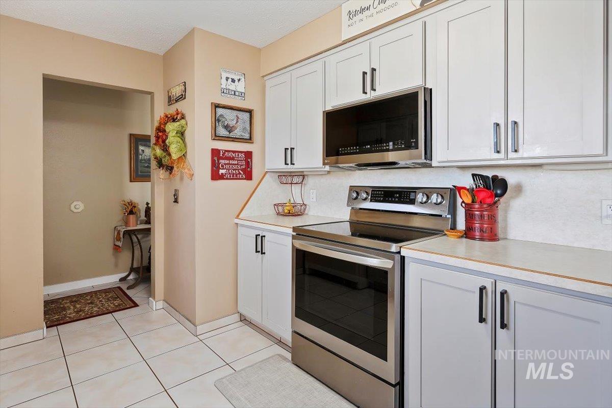 Kitchen with stainless steel appliances, light countertops, light tile patterned floors, and white cabinetry
